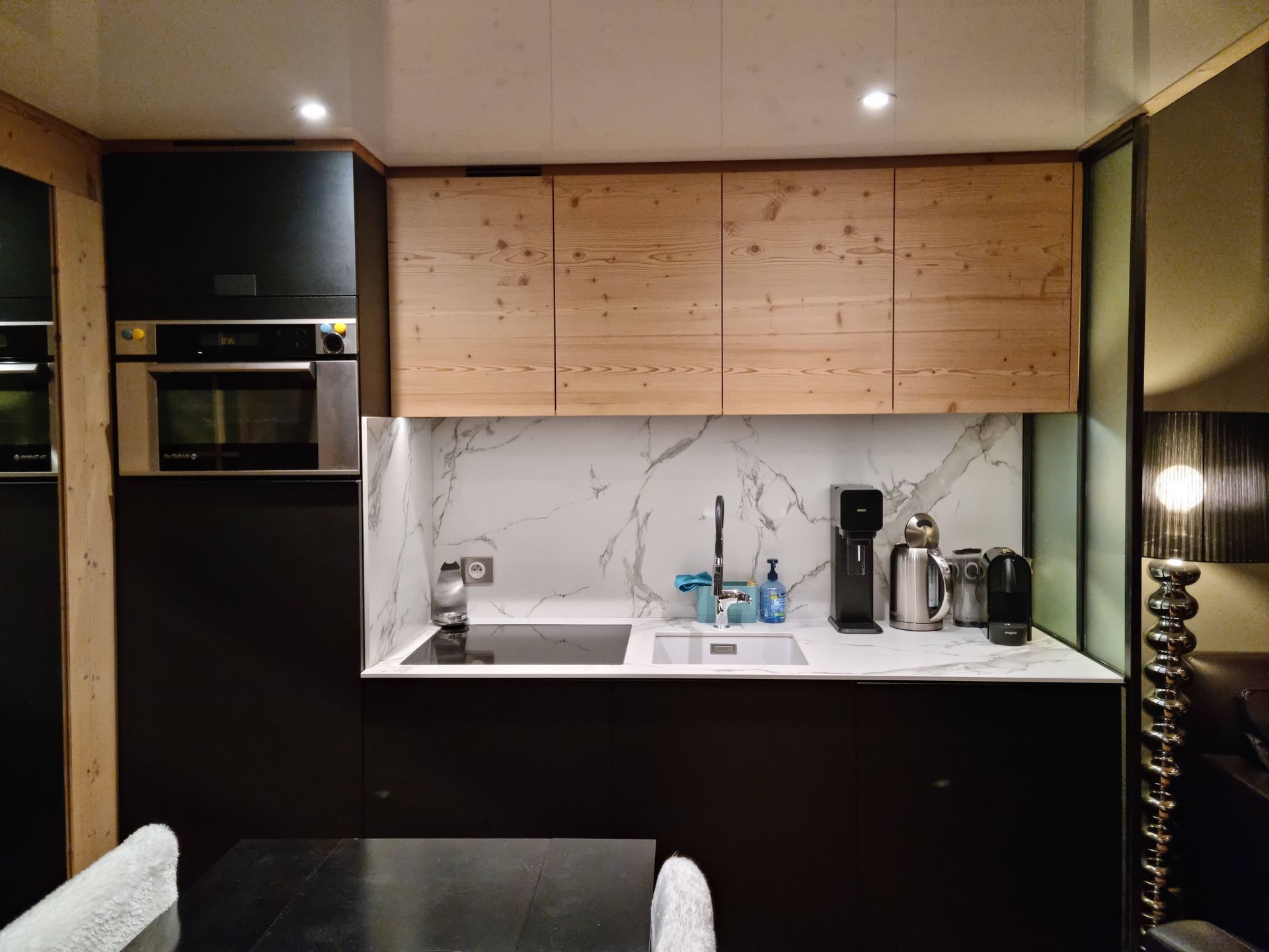 Cuisine moderne avec armoires noires et en bois, crédence en marbre et appareils électroménagers en acier inoxydable.