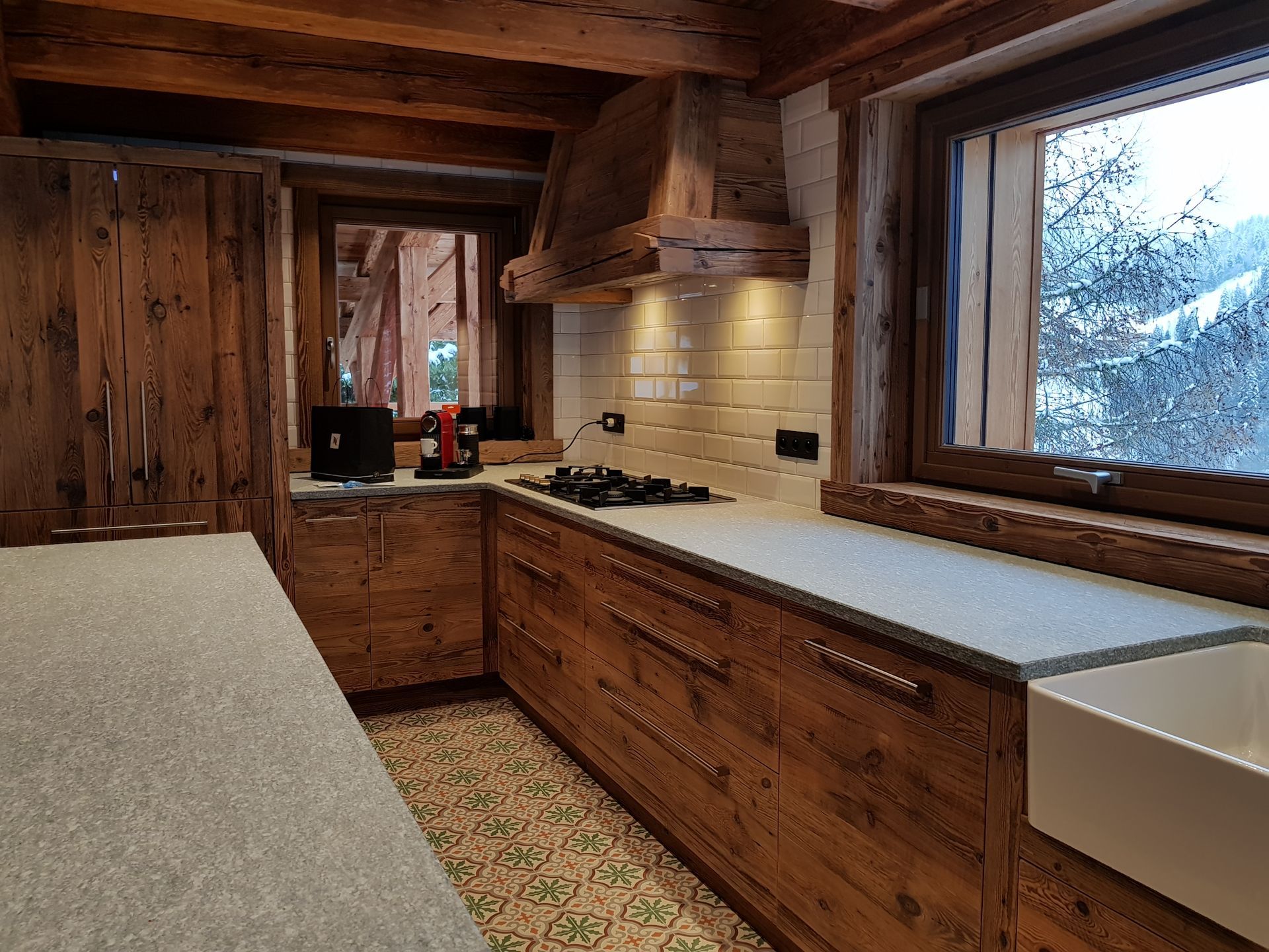 Cuisine rustique en bois avec plans de travail blancs et une fenêtre donnant sur un paysage enneigé.