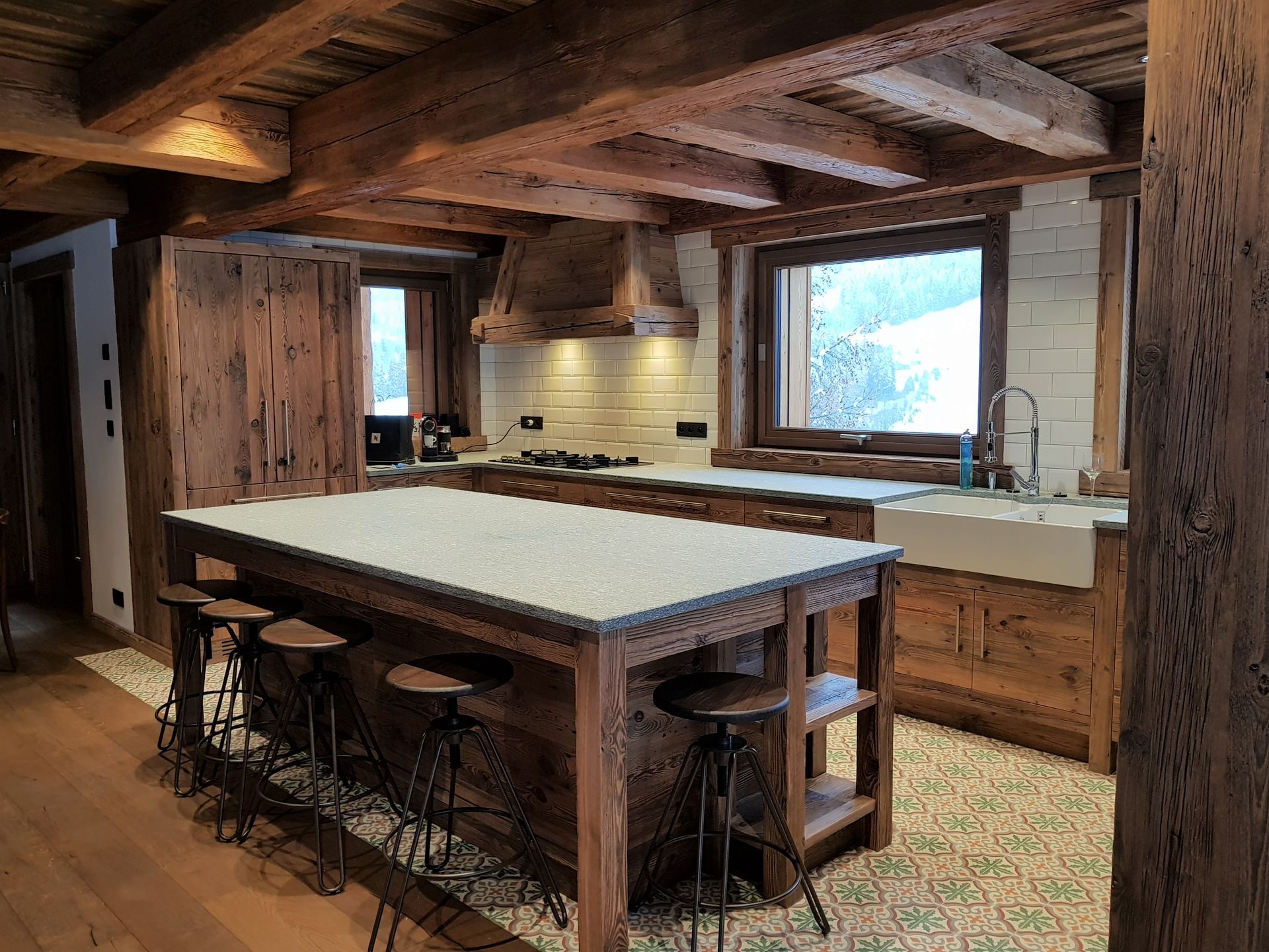 Cuisine rustique avec poutres apparentes, îlot central avec tabourets et plans de travail blancs.