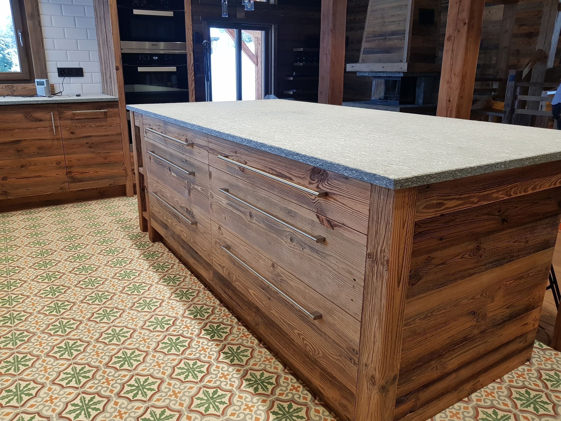 Îlot de cuisine en bois avec plan de travail gris, installé dans une pièce au sol carrelé à motifs.