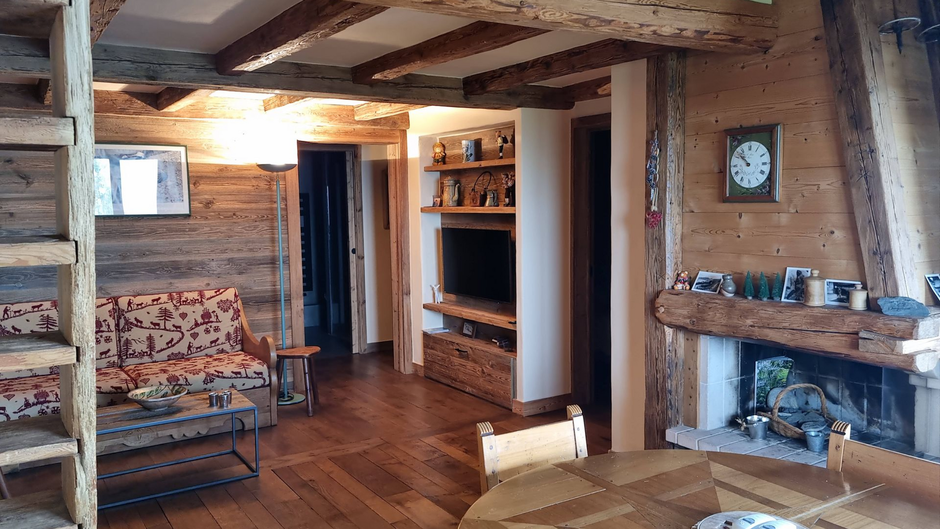 Intérieur chaleureux de chalet en bois avec canapé, cheminée, télévision et poutres apparentes.