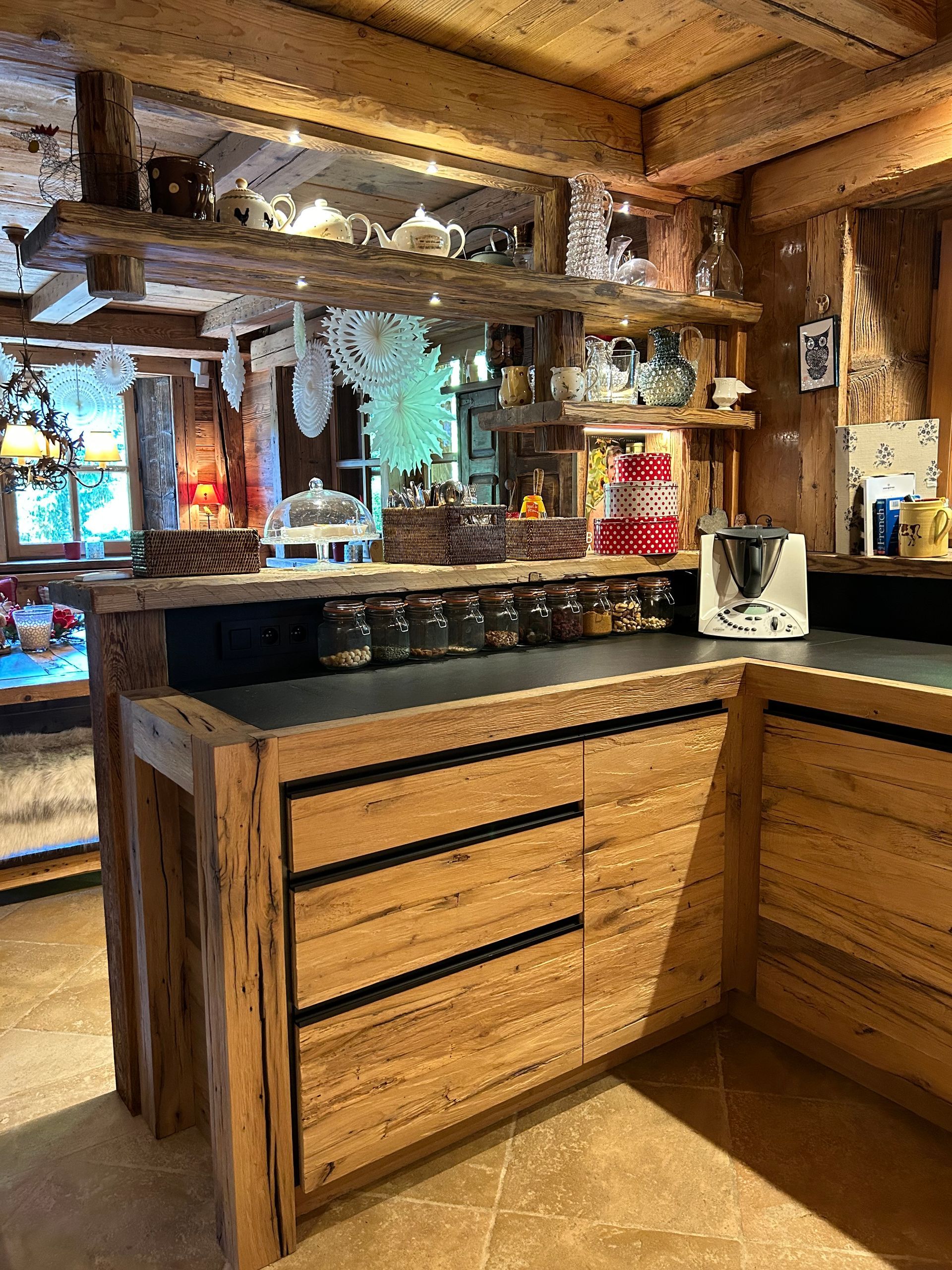 Cuisine en bois avec étagères ouvertes, pots à épices et plan de travail.