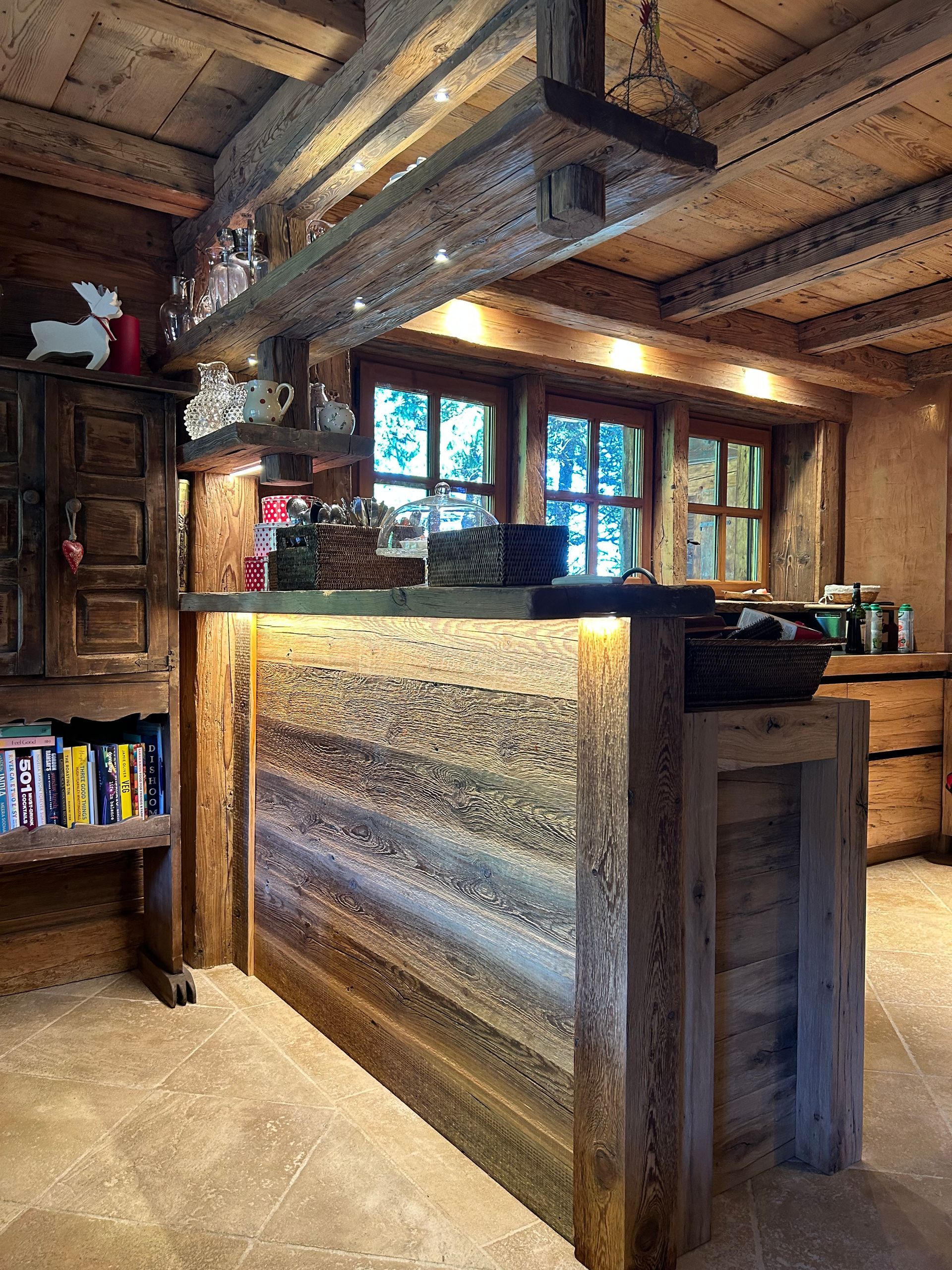 Cuisine rustique avec placards, plan de travail et poutres en bois. Une fenêtre apporte de la lumière naturelle.