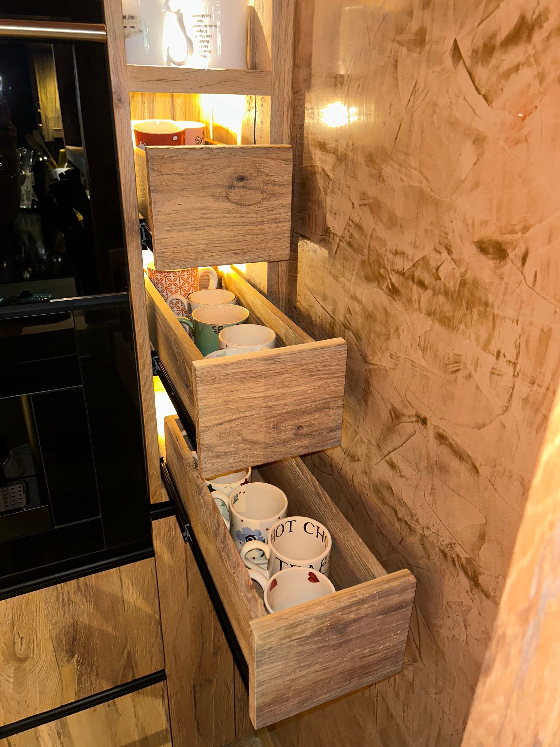 Des tiroirs en bois encastrés dans un mur, remplis de tasses et de soucoupes.