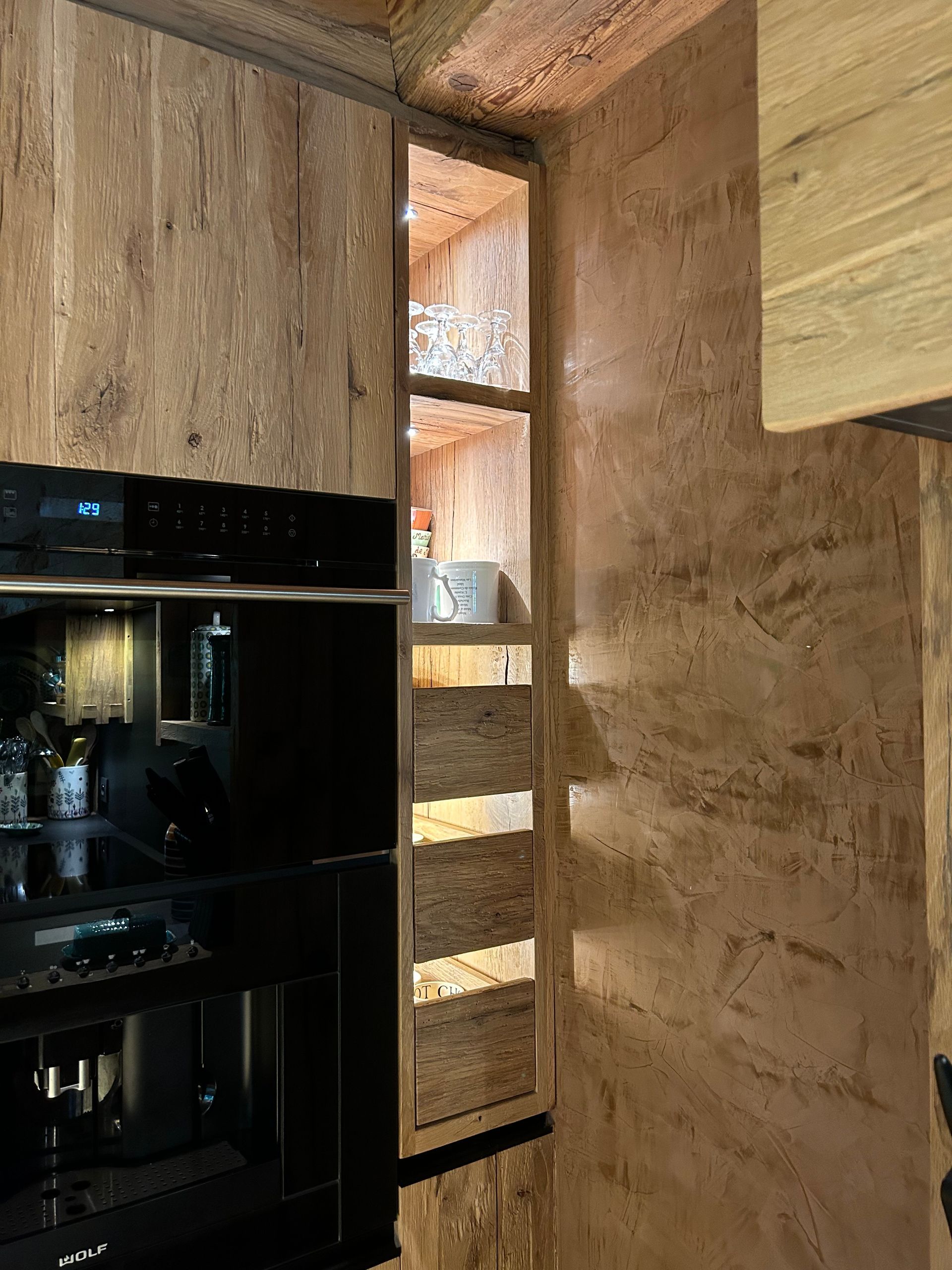 Cuisine équipée avec rangements et appareils électroménagers intégrés, comprenant une étagère encastrée fine éclairée de l'intérieur. Murs aux tons bois naturels.