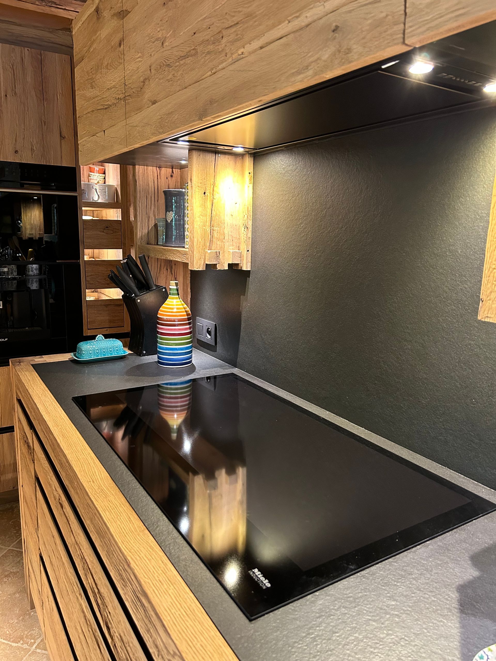 Cuisine avec plaque de cuisson noire, placards en bois et crédence grise.