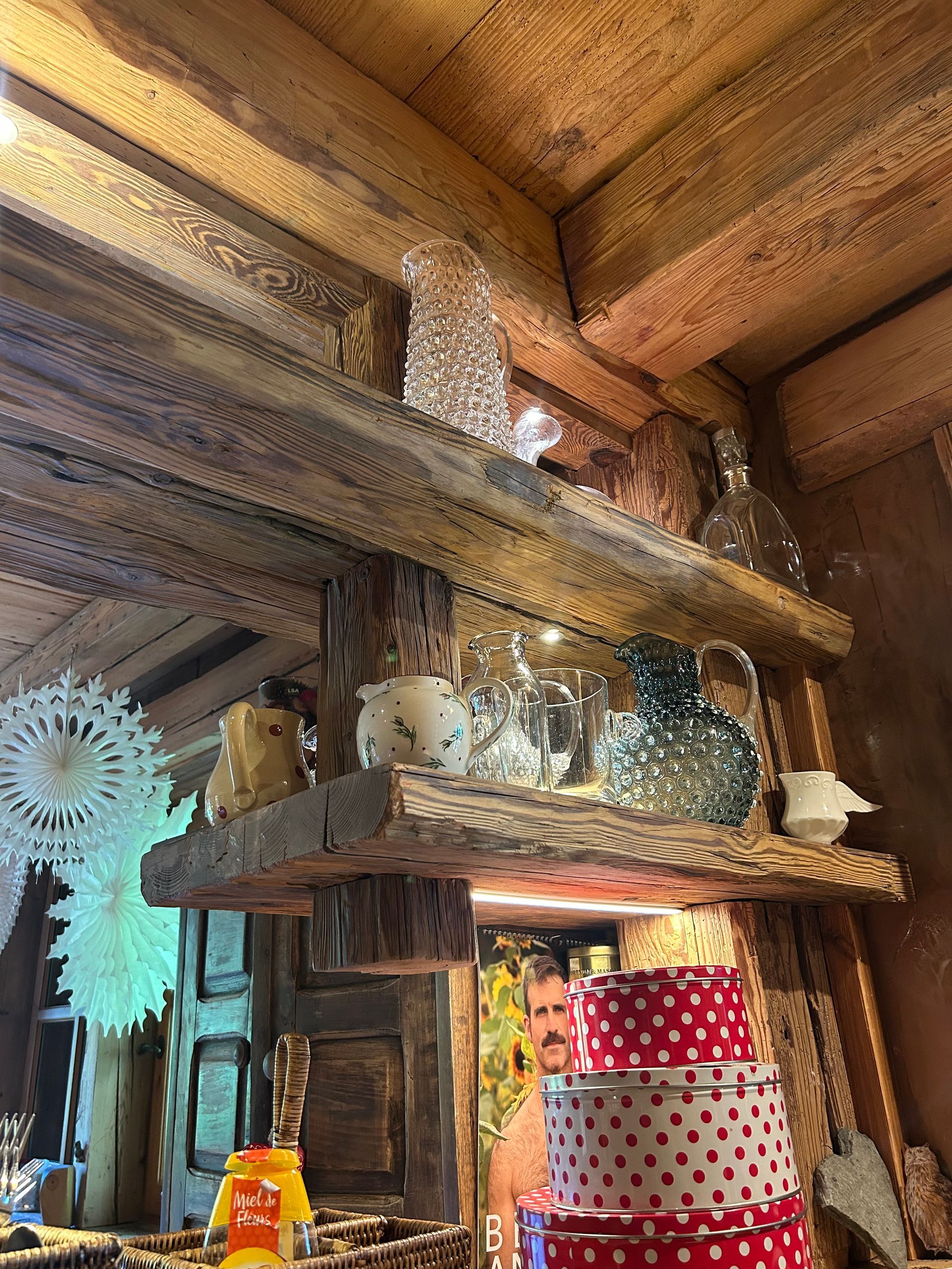 Des étagères en bois présentent divers objets décoratifs : vases, pichets et boîtes, dans un intérieur rustique.