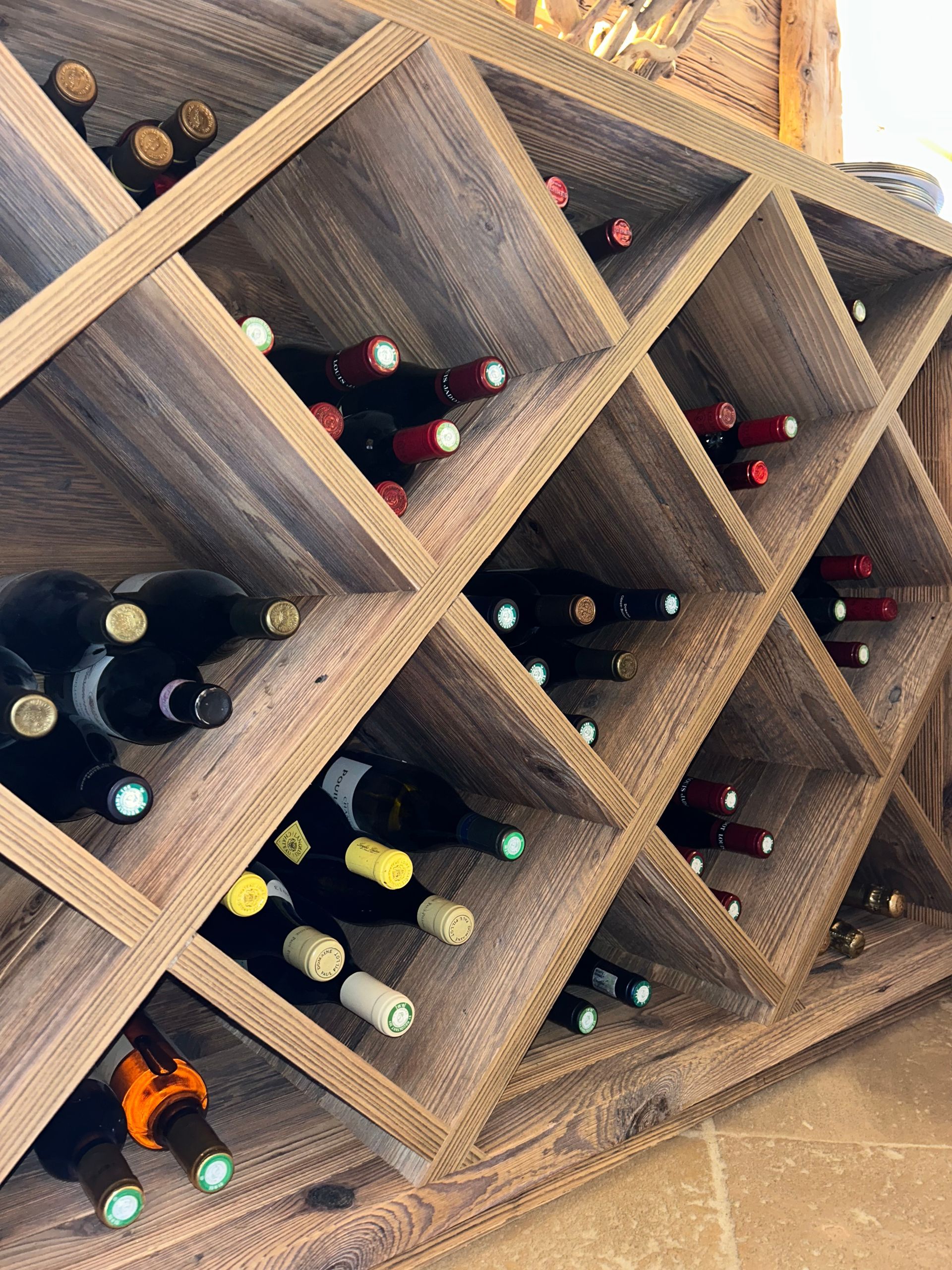 Casier à vin en bois en forme de losange, rempli de bouteilles de vin variées dans un cadre rustique.