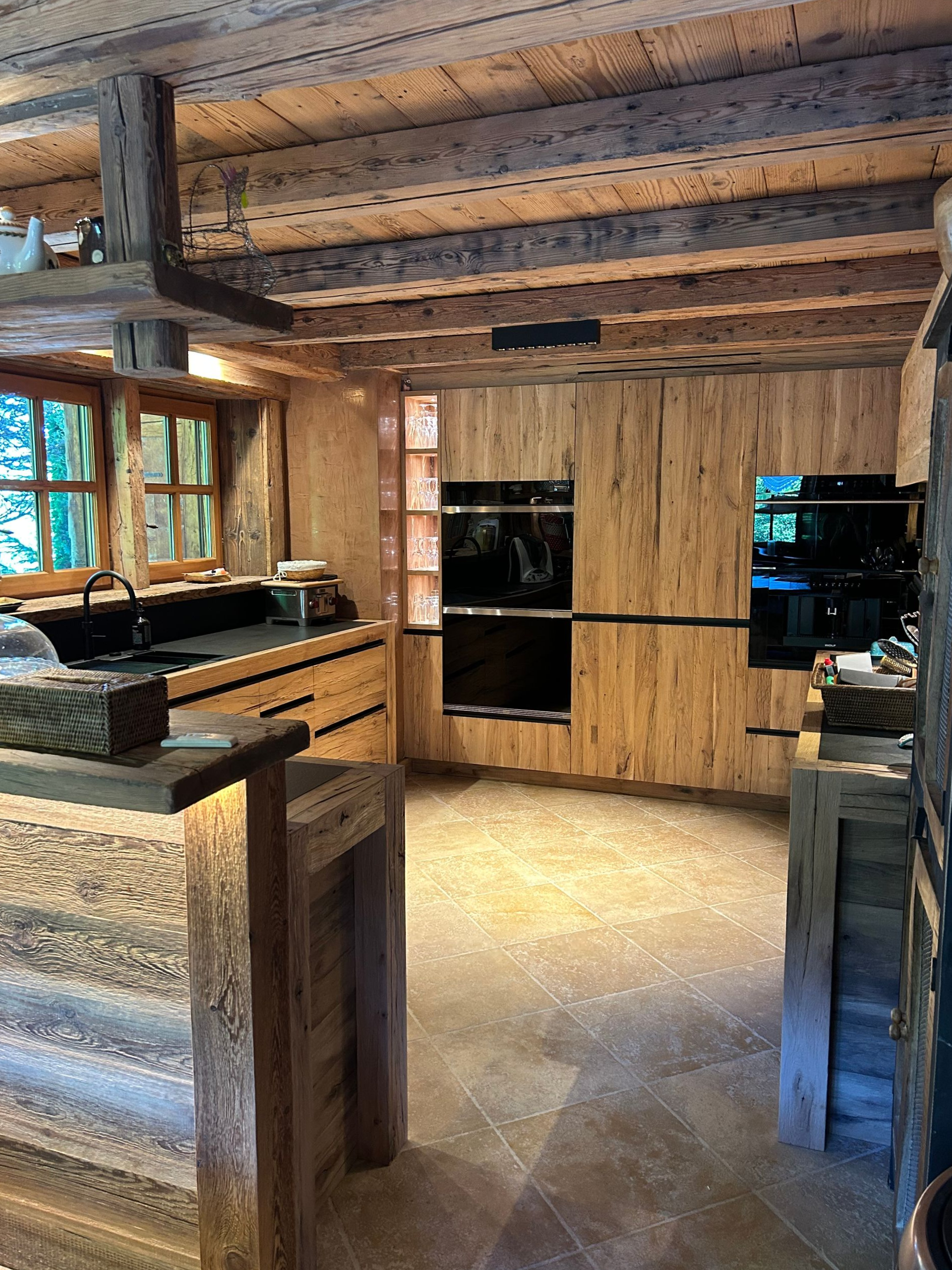 Cuisine en bois avec fours encastrés, murs lambrissés et poutres apparentes.