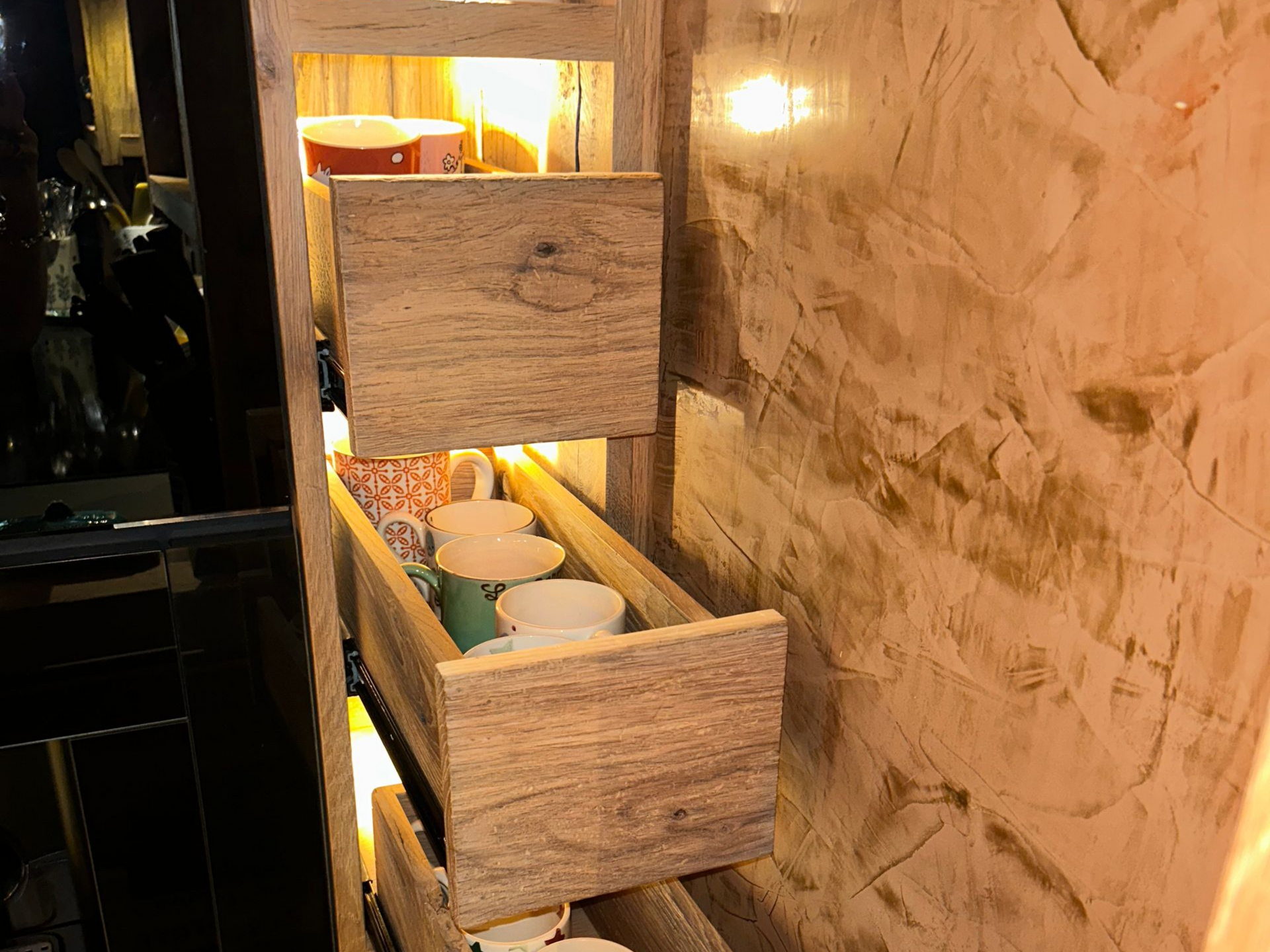 Tiroirs en bois dans un meuble de cuisine, éclairés par une lumière chaude.