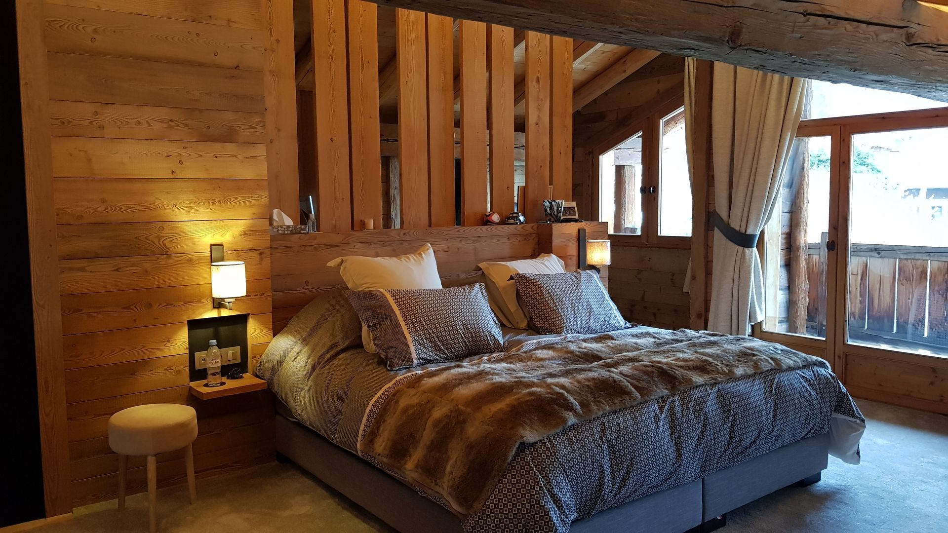 Chambre confortable avec murs en bois, lit recouvert de fausse fourrure et balcon.