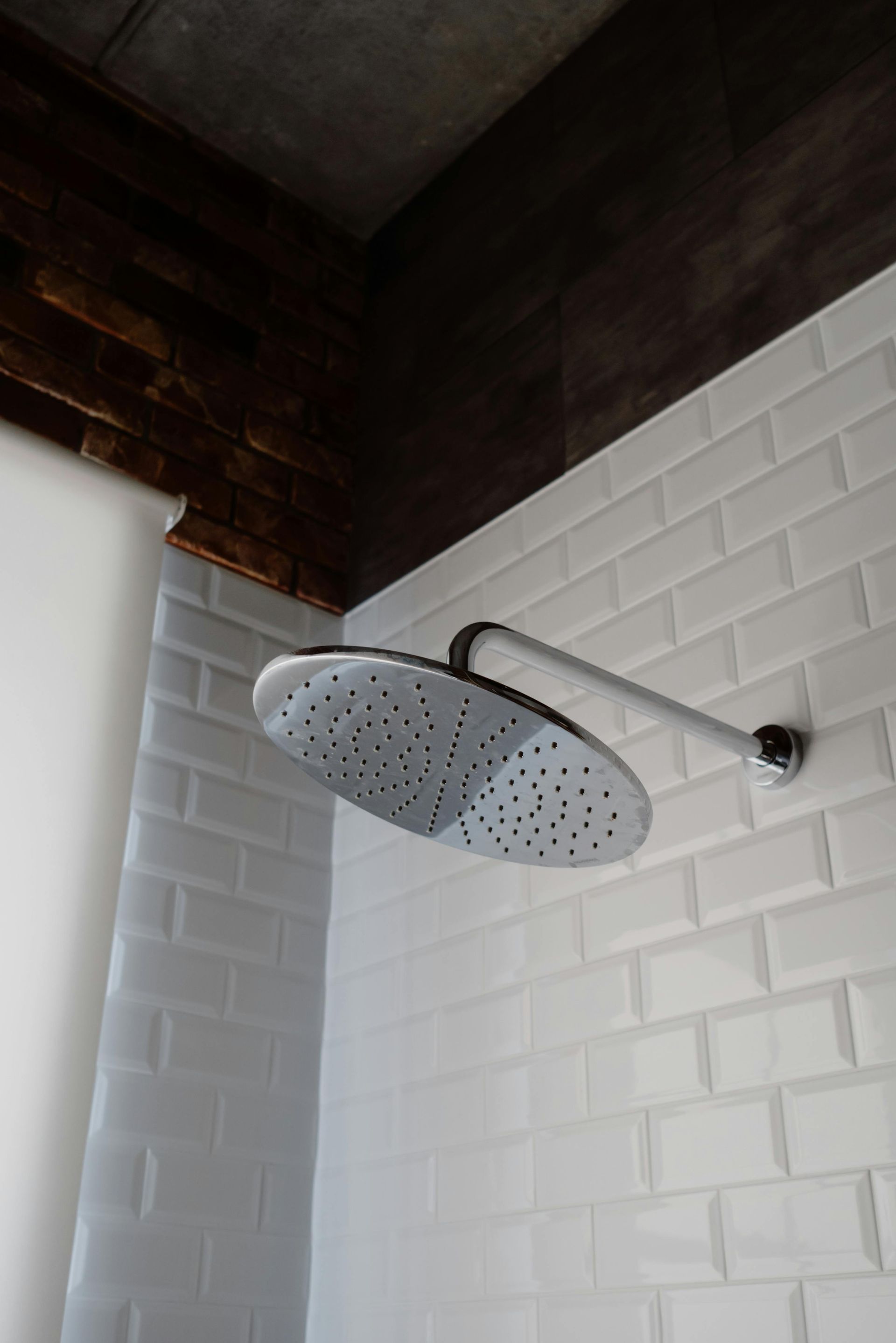 White tiled shower wall with large circular rain shower head.