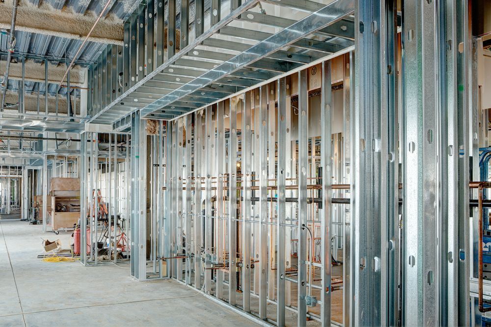 Interior view of a building under construction, showing exposed metal framing for walls and ceiling, and pipes.