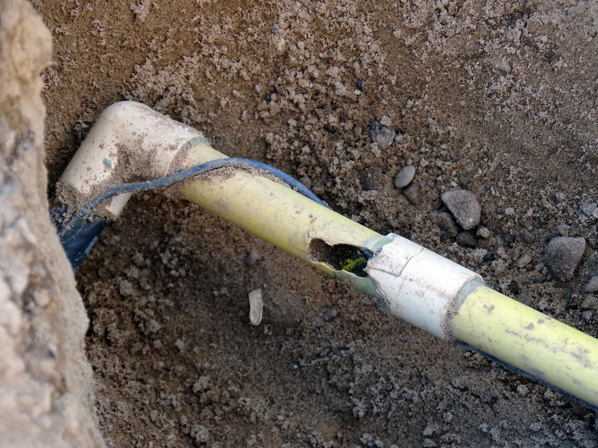 Damaged yellow pipe in dirt, with a hole and exposed interior.