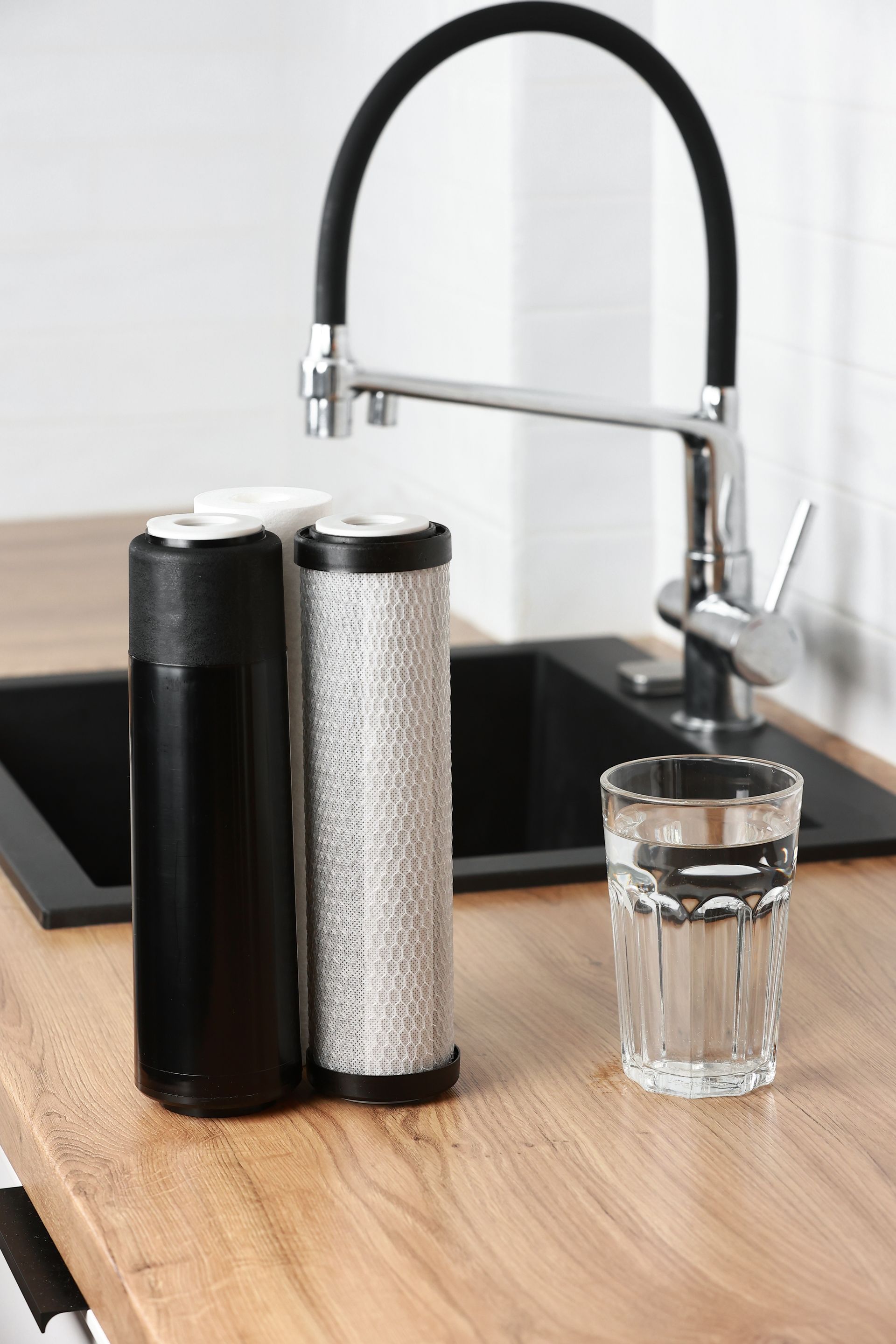 Water filter system next to a sink with a glass of water on a wooden countertop.