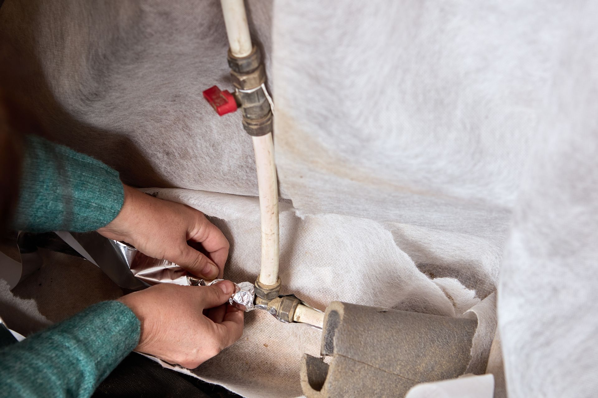 Hands working on plumbing pipes wrapped in insulation in a wall.