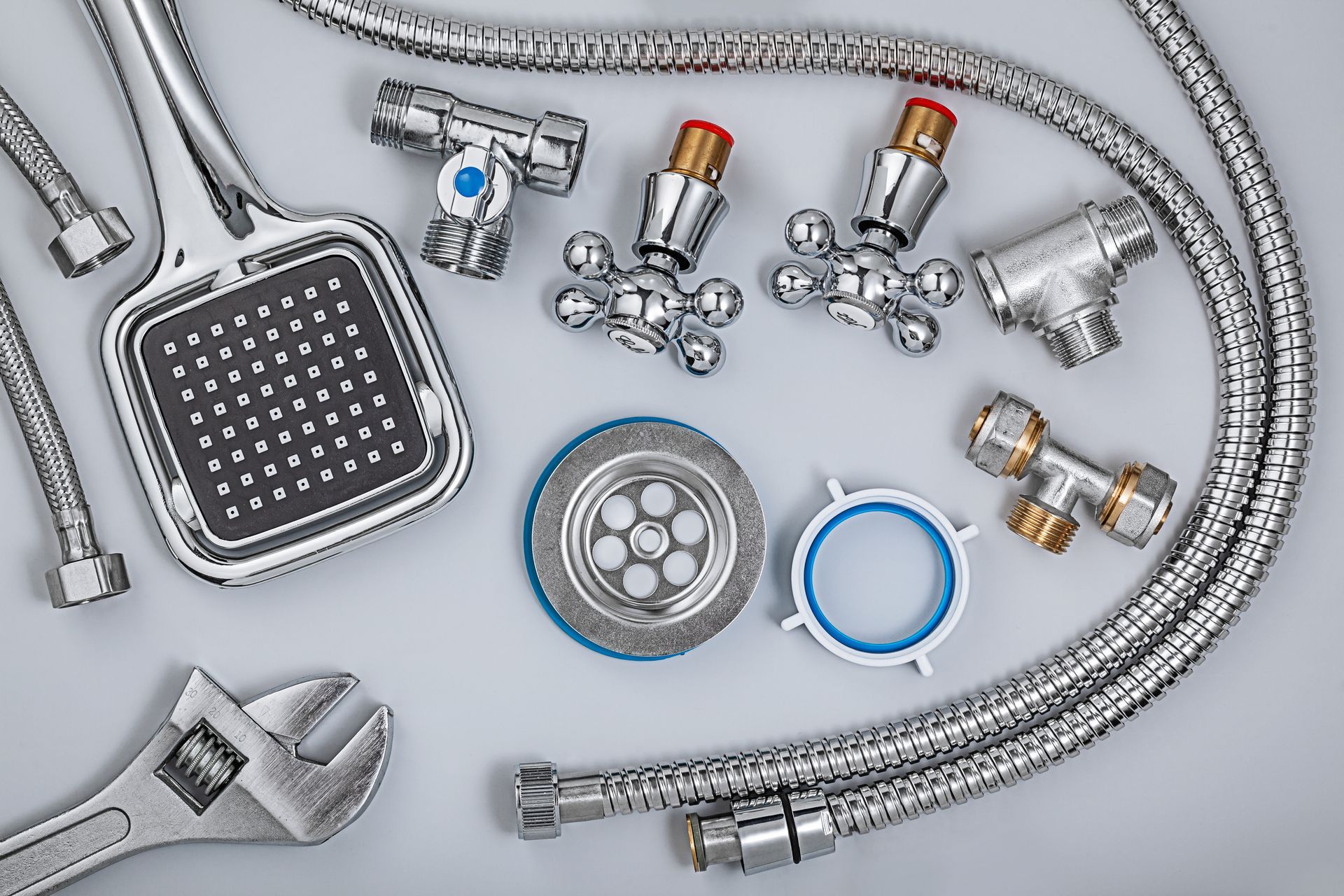 Plumbing fixtures: showerhead, faucet handles, metal hoses, drain strainer, wrench, on white surface.