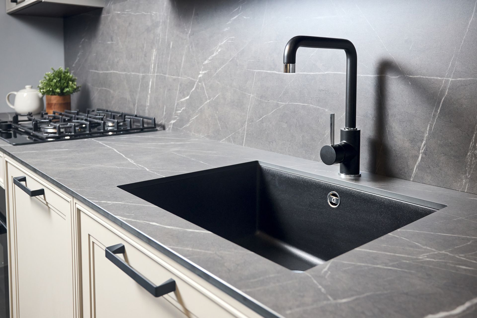 A kitchen sink with a black faucet and gray countertop, with a gas stove and cabinet handles.