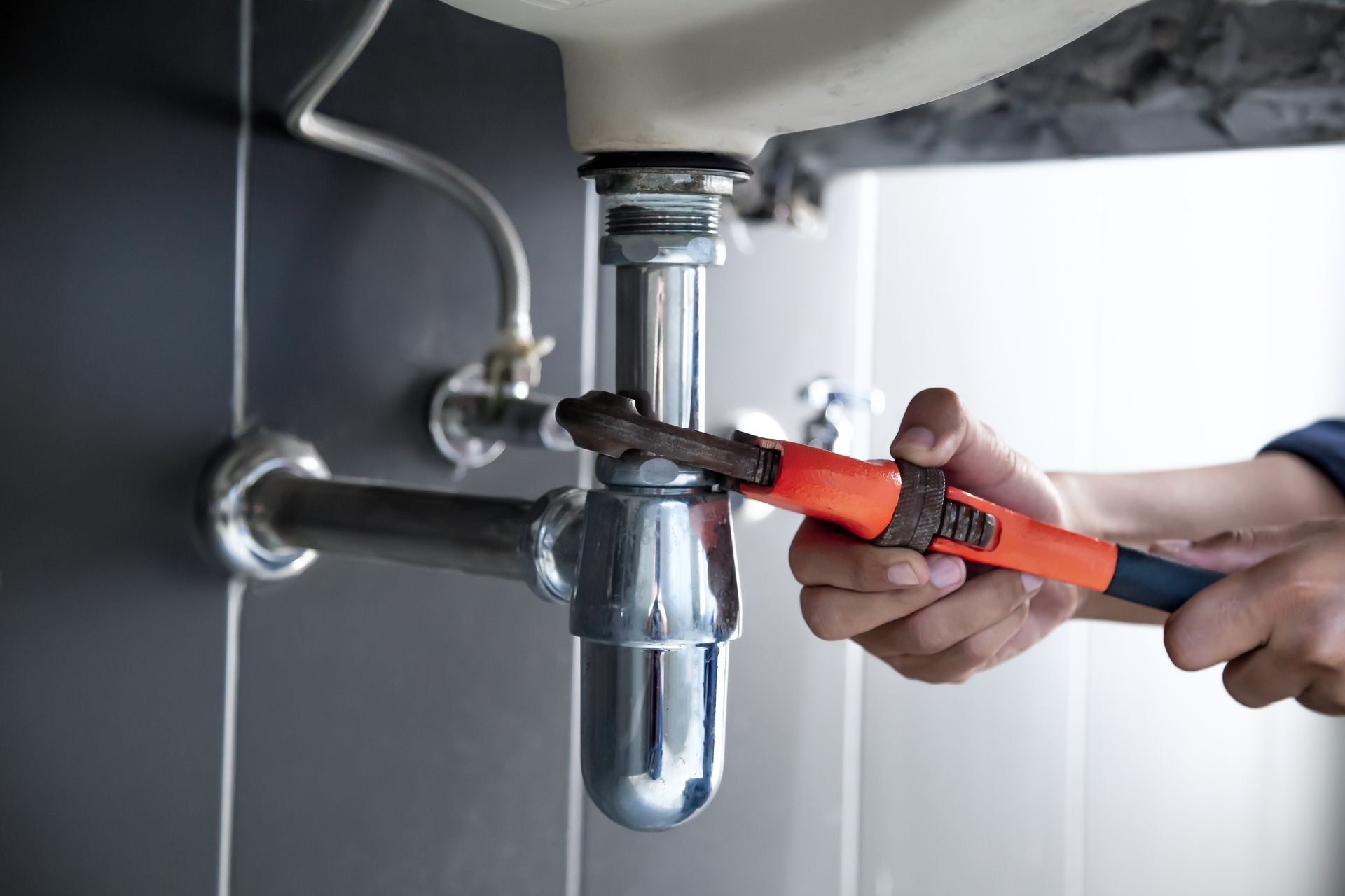 Person using a wrench on plumbing under a sink.
