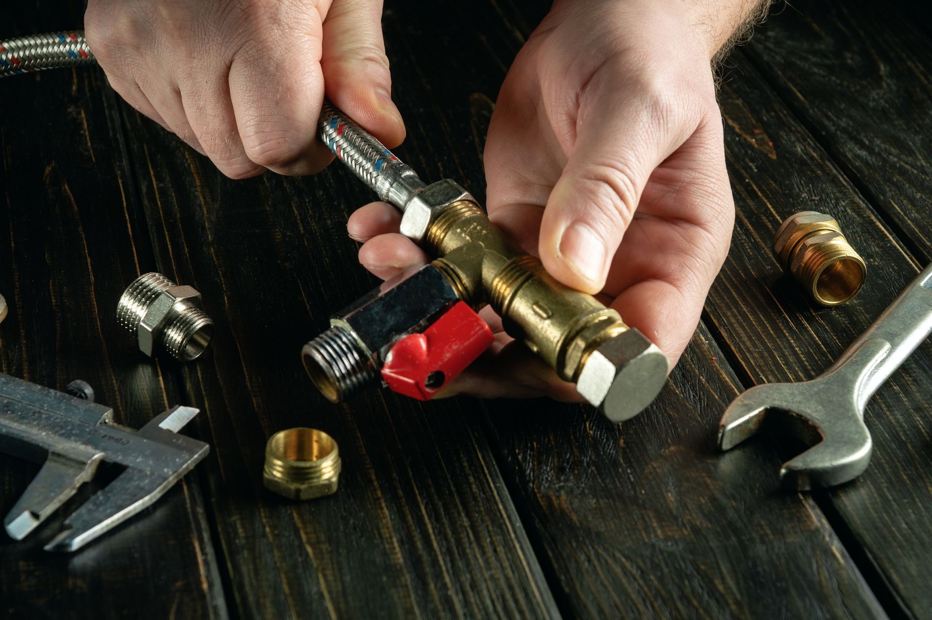 Hands assembling plumbing components with tools on a wooden surface.