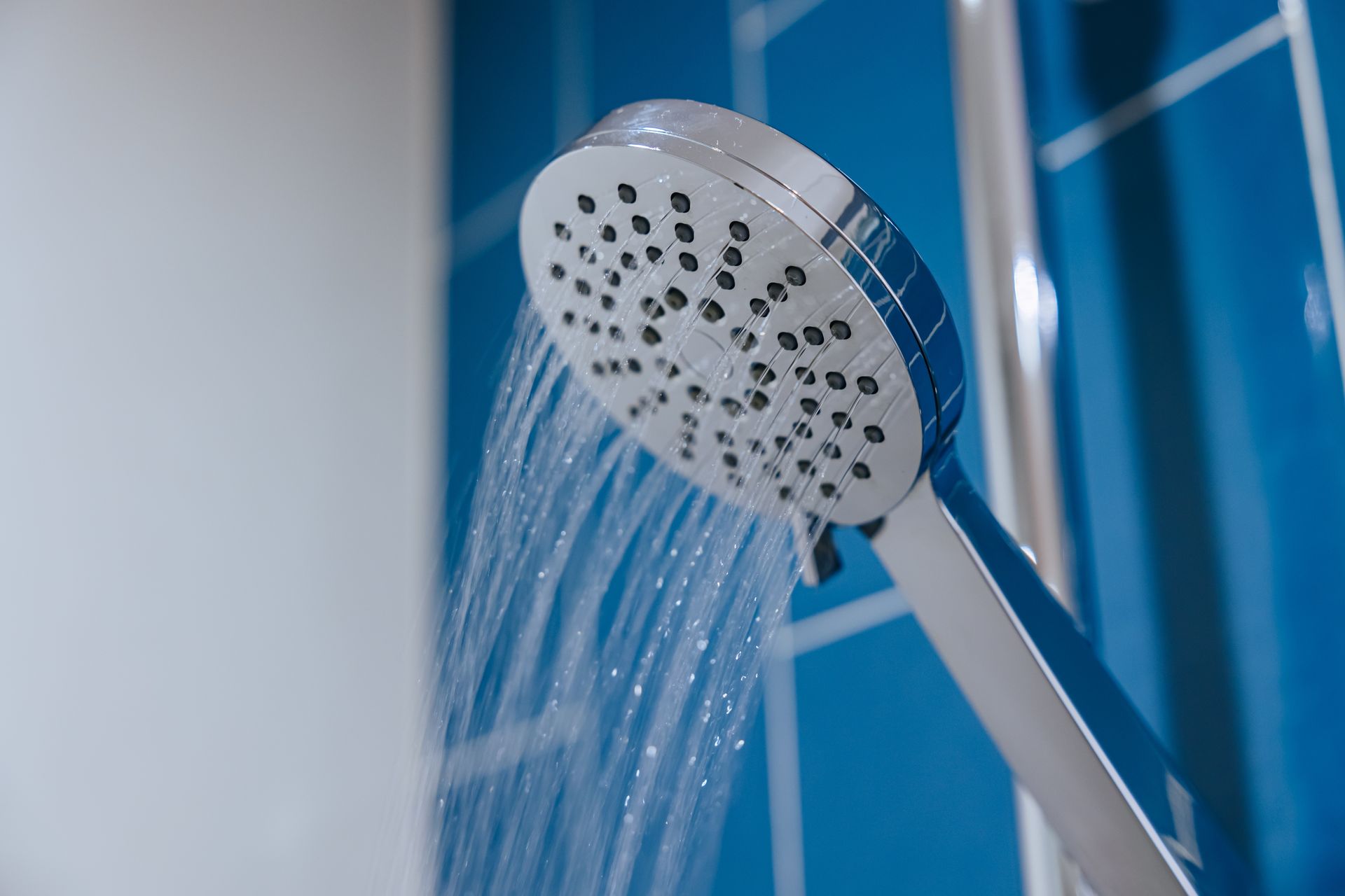 Chrome showerhead spraying water with blue tile wall in background.
