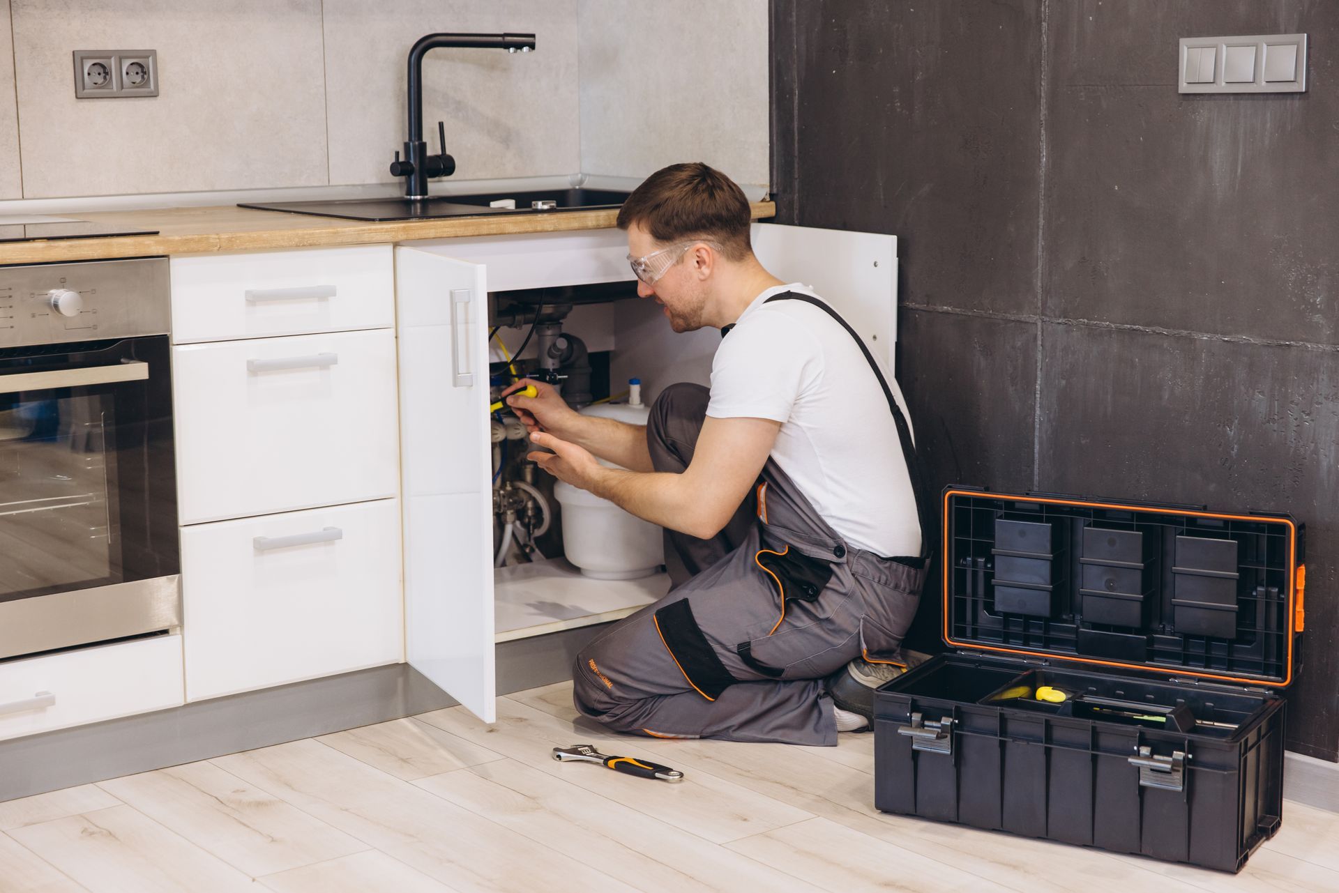 Plumber working under a kitchen sink, tools in an open toolbox nearby.