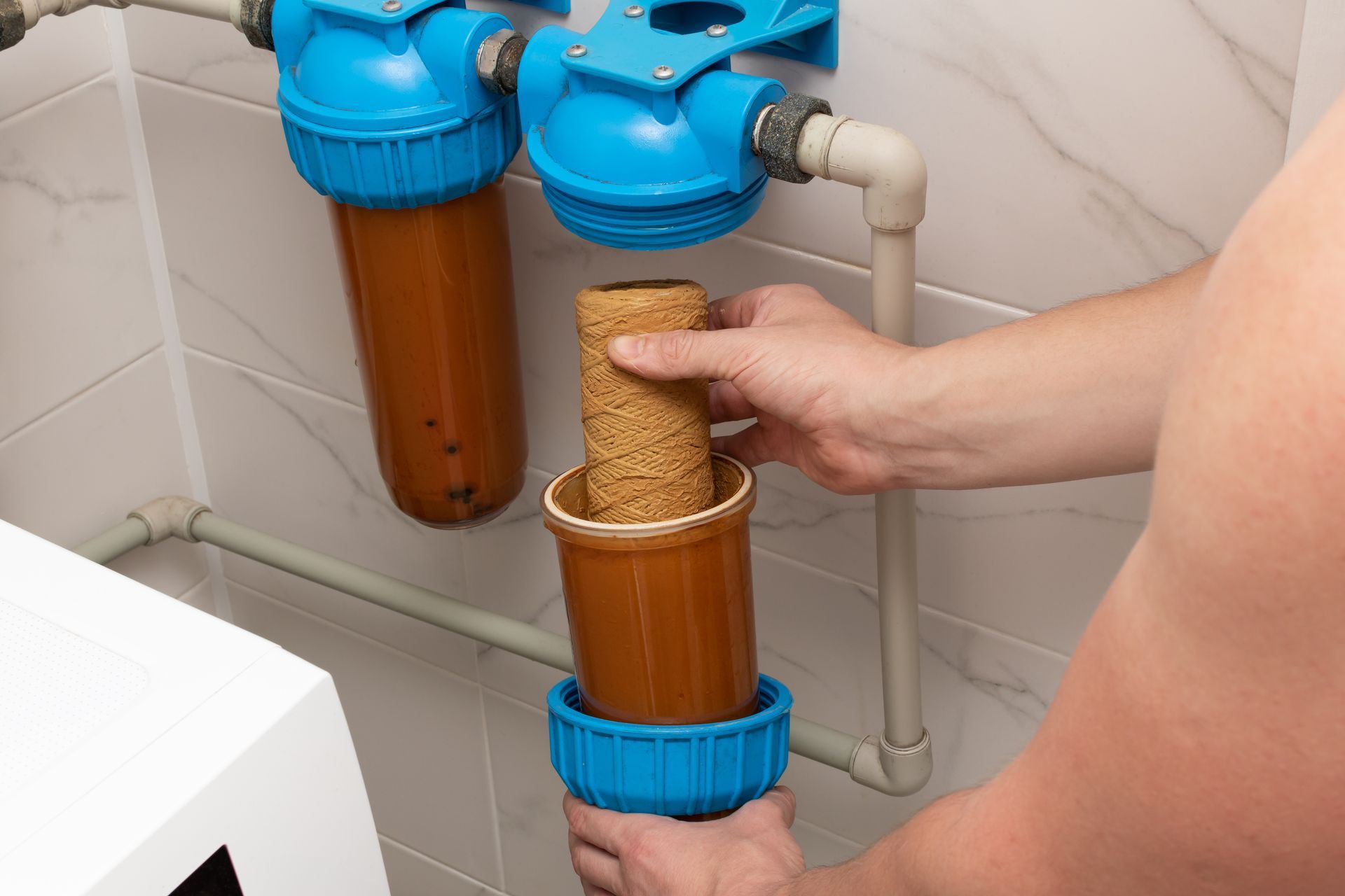 A person replacing a dirty water filter in a two-stage blue filtration system.