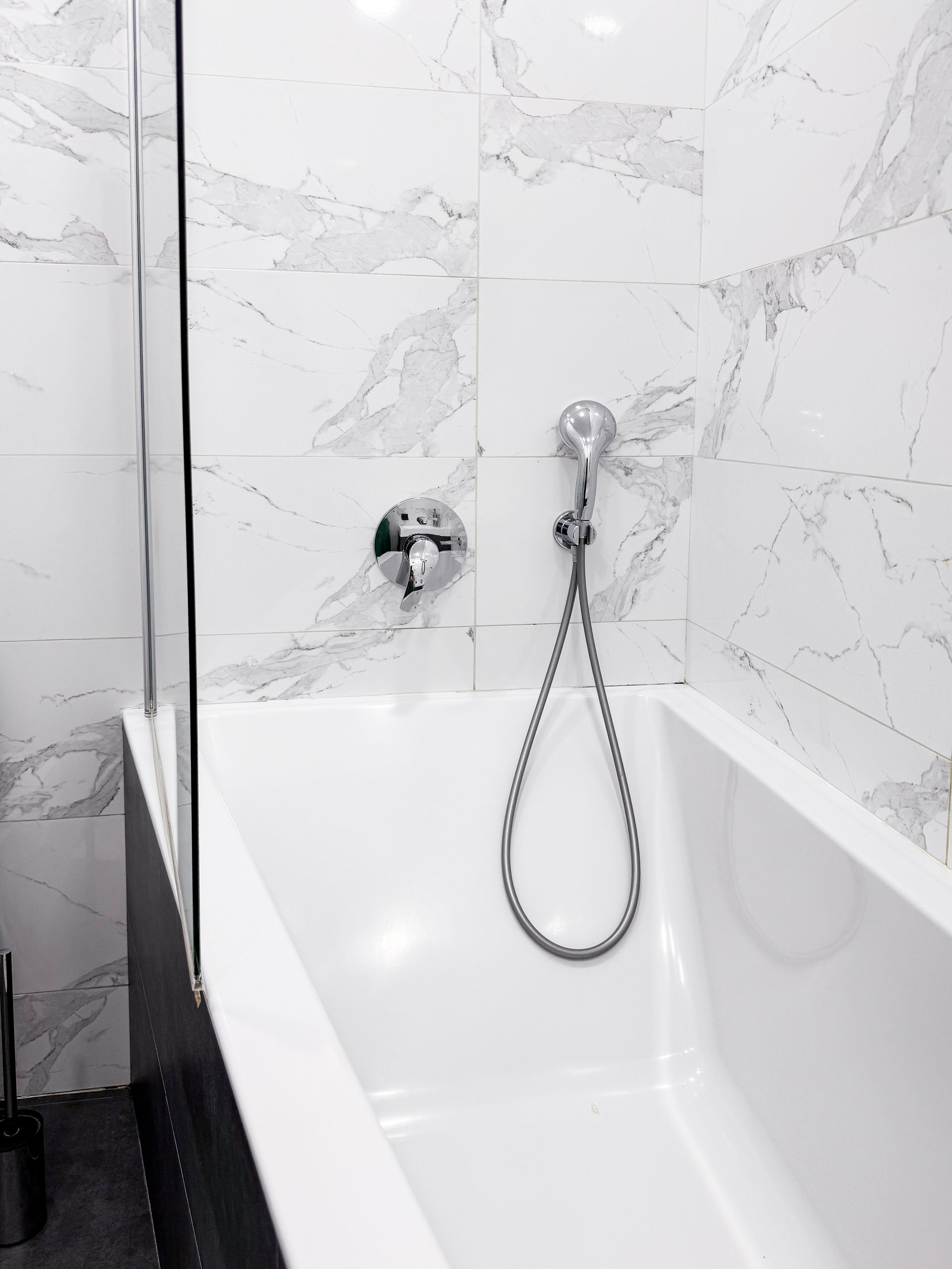 White bathtub with showerhead and faucet against marble tiled wall.