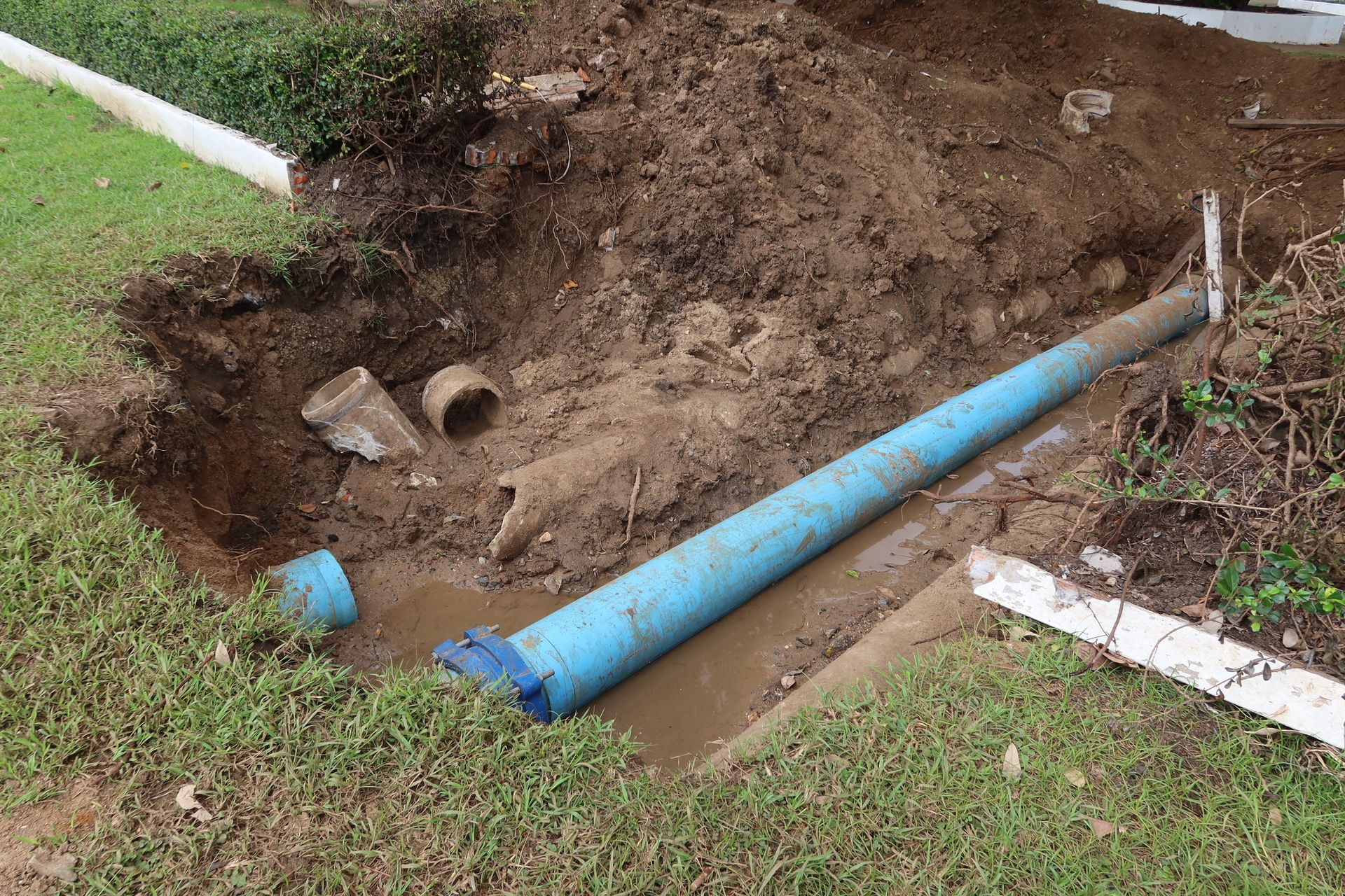 A blue pipe in an excavated trench in a yard, with dirt and another broken pipe visible.