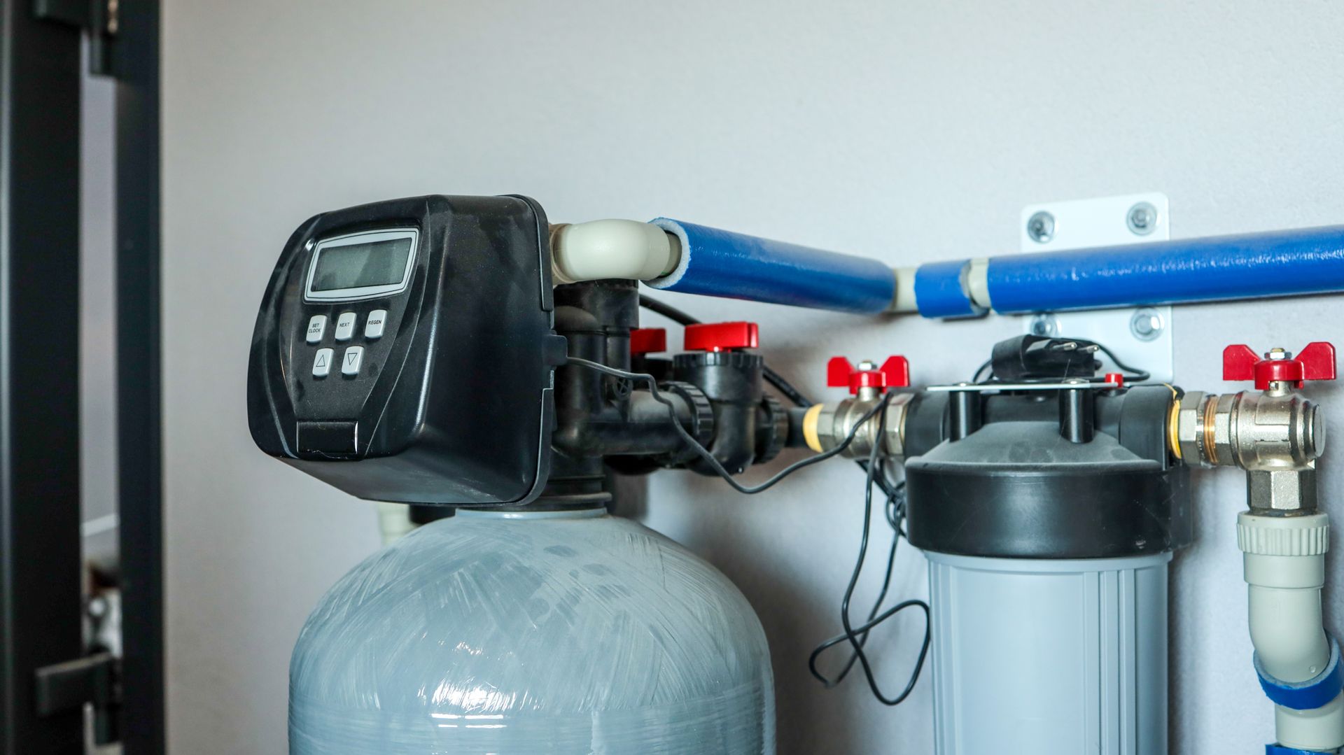 Water filtration system with digital display, tanks, and plumbing against a wall.