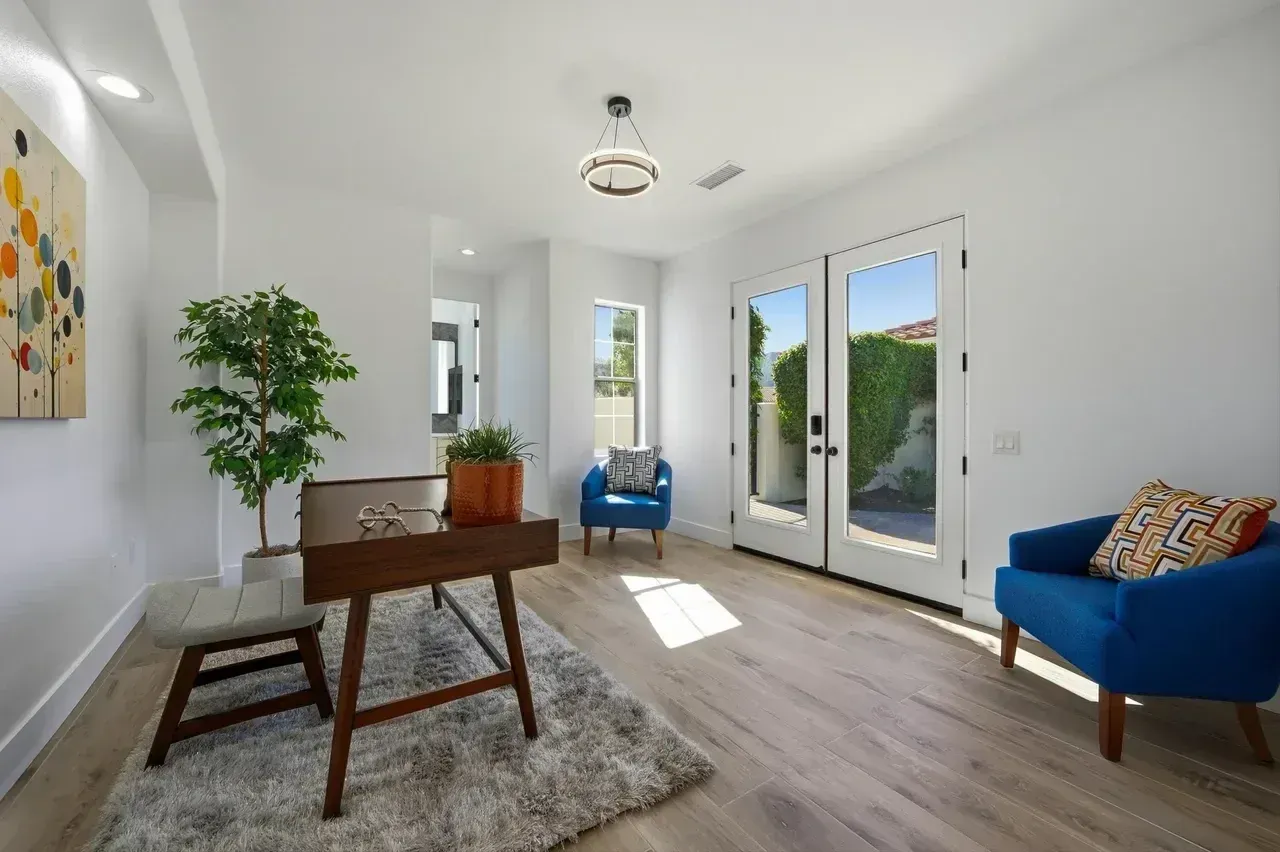 Bright office space with desk, two blue chairs, French doors, and a small potted tree.