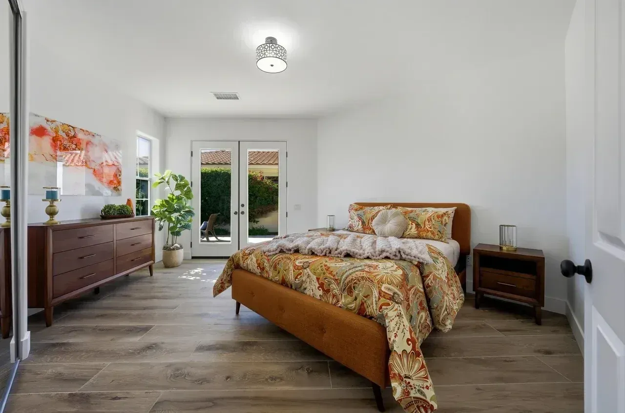 Bedroom with wooden furniture, including a bed and dresser, and double doors to a garden.