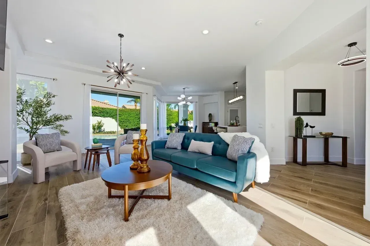 Bright living room with teal sofa, wooden floors, and outdoor view.
