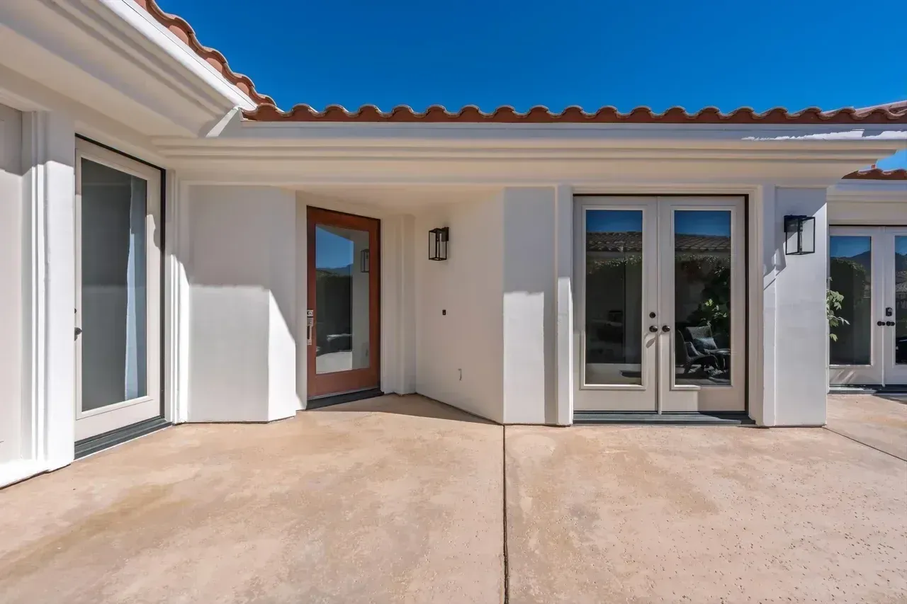 Exterior of a white stucco building with terracotta roof tiles, open doorway, and glass doors on a concrete patio