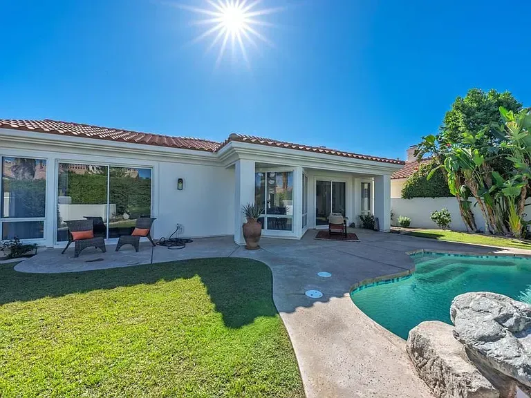 Backyard with a pool, patio, and white house under a bright sun.
