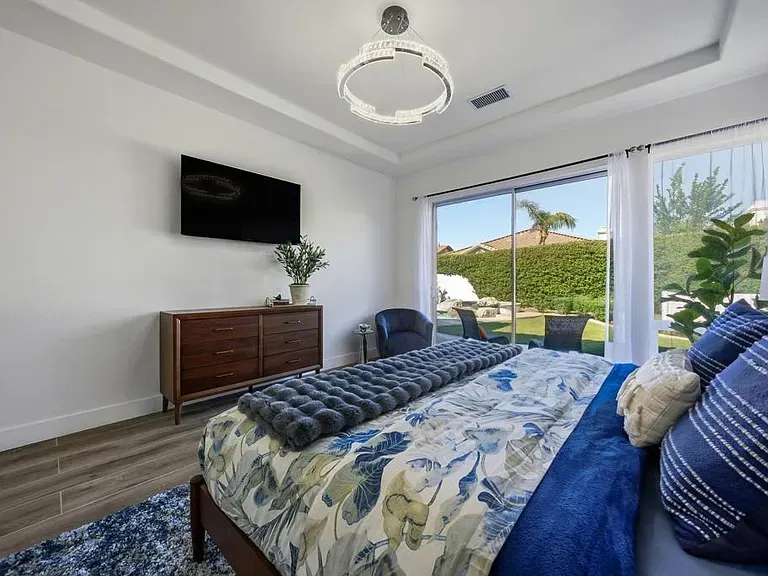 Bedroom with bed, TV, dresser, and sliding glass doors overlooking a backyard with pool.