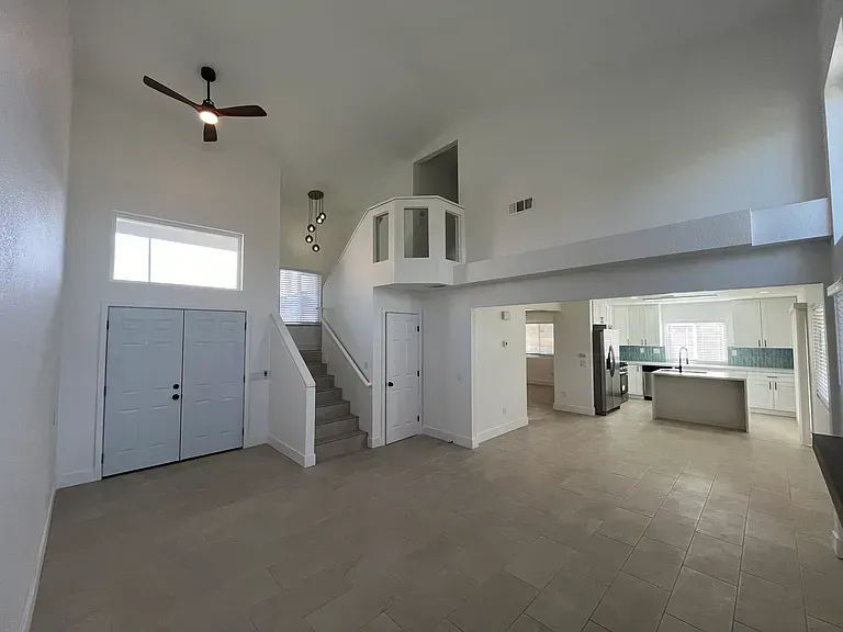 Spacious, white-walled living area with a staircase, kitchen, and a loft.