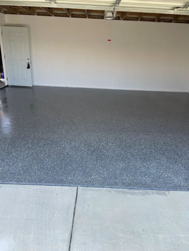 A garage with a gray speckled epoxy floor, white walls, and a white door.