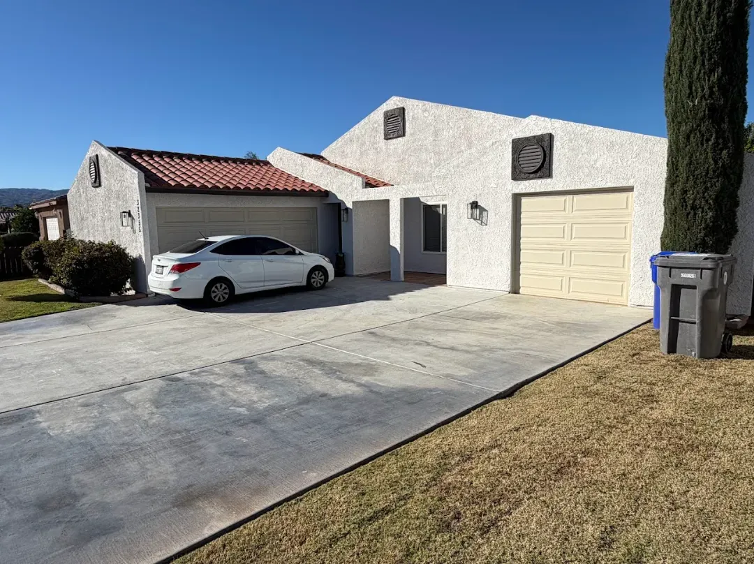 White stucco house with red tile roof, two-car garage, white car in driveway, clear blue sky.