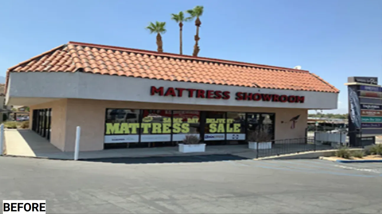 Exterior of a Mattress Showroom with sale signage. Tan building, red tile roof, and palm trees.