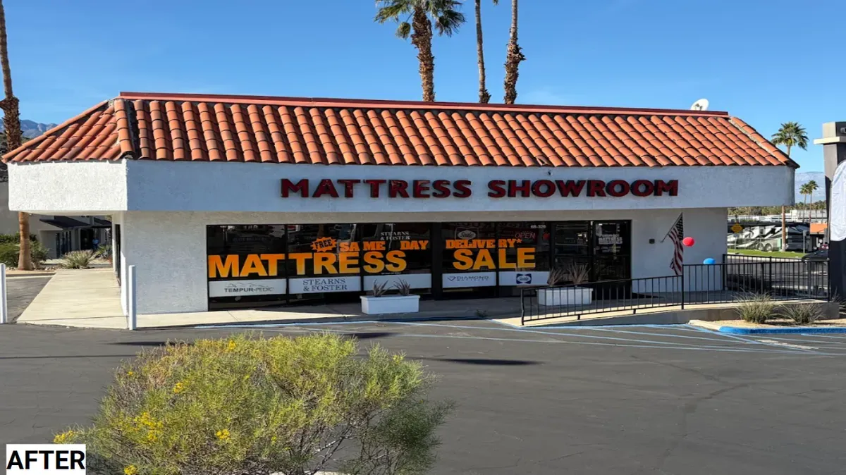 A mattress showroom in a single-story building. Red tile roof, large windows, and sale signs.