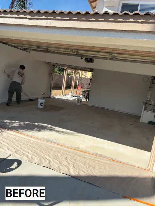 Person painting the interior garage walls with a roller. Garage floor covered with brown paper.