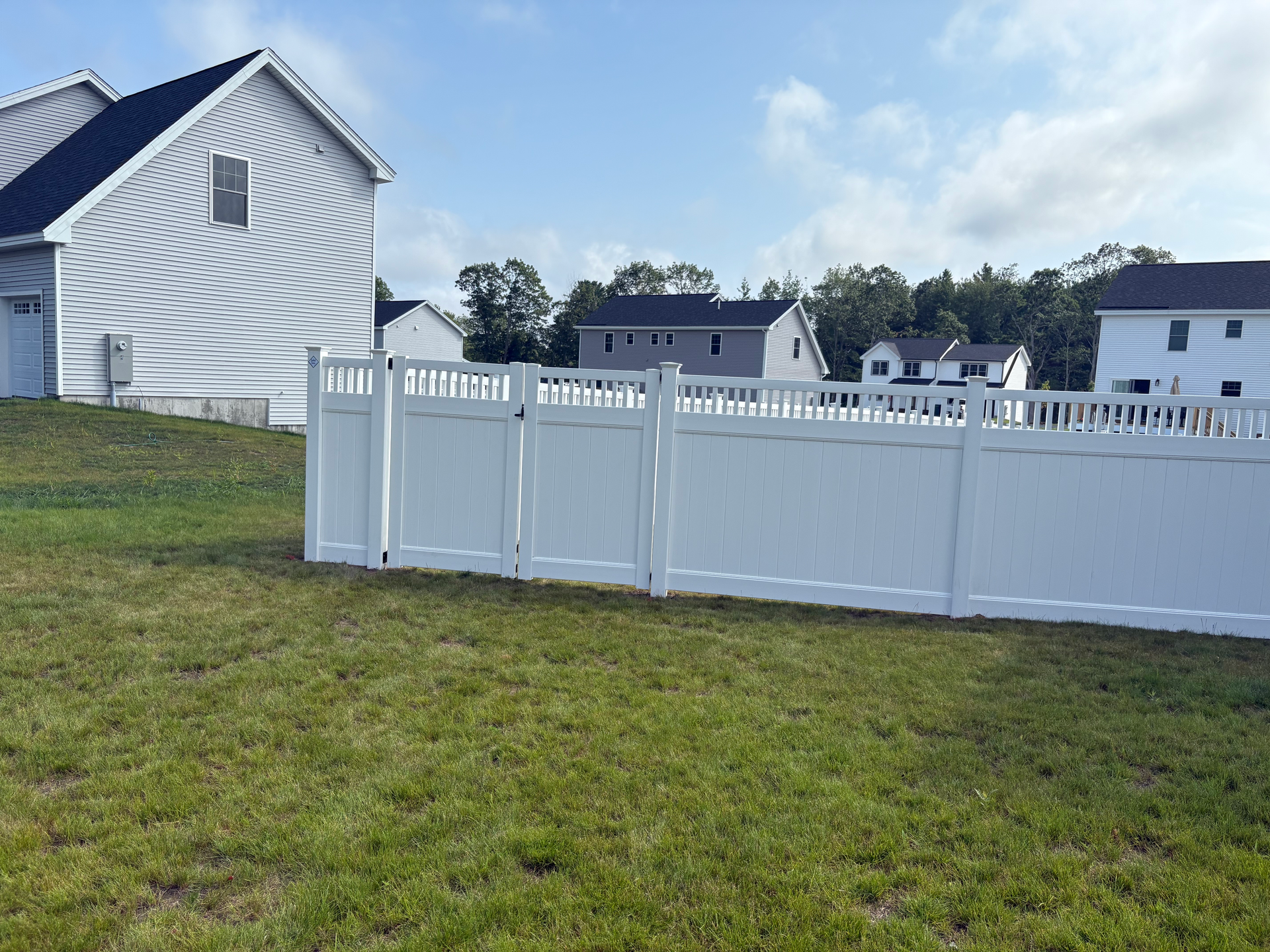 A white fence surrounds a lush green field in front of a house.
