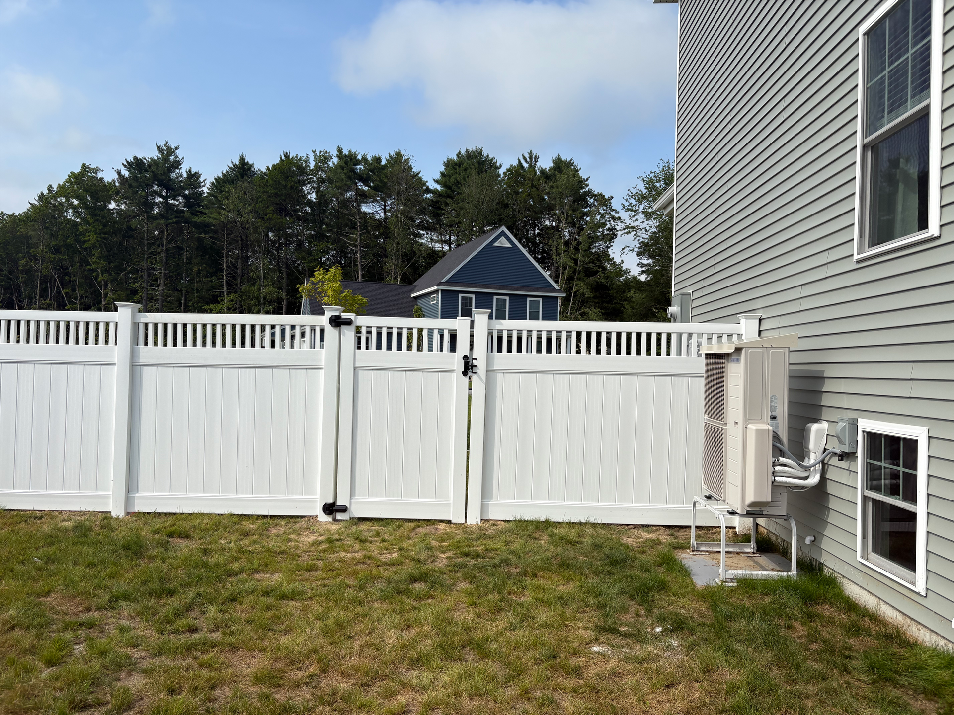 A white fence with a gate is in the backyard of a house.