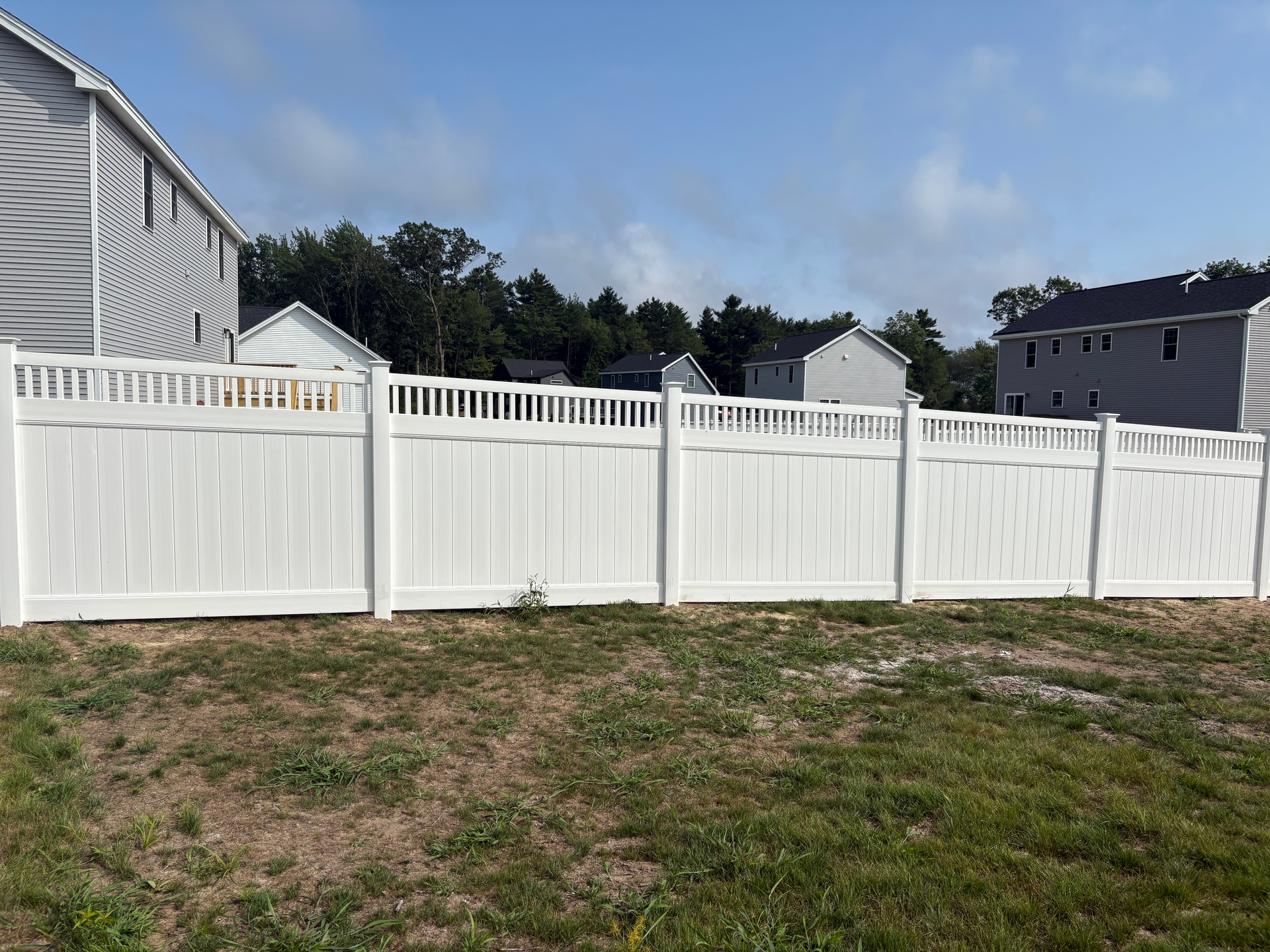 A white fence surrounds a grassy field in front of a house.
