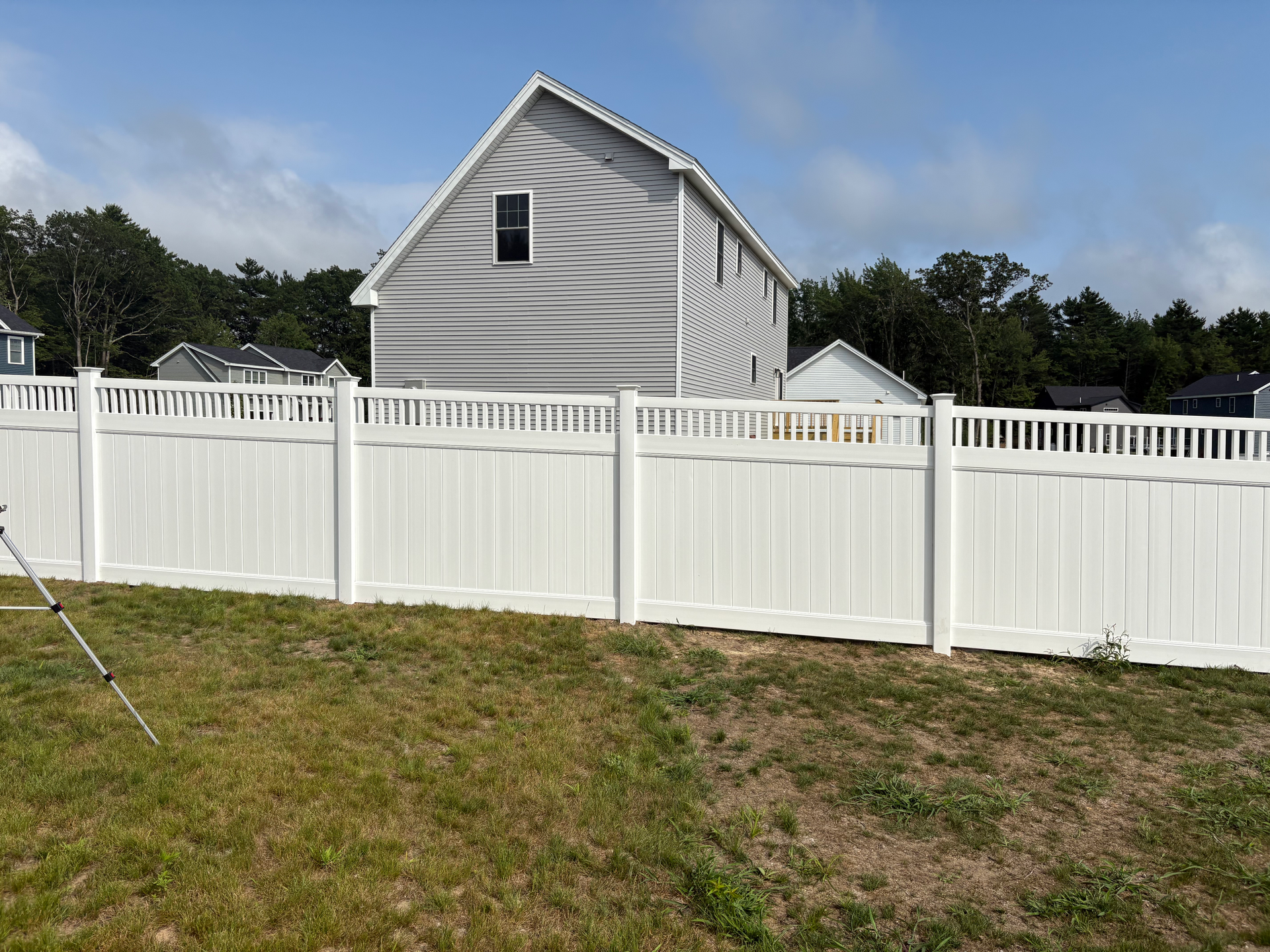 A white fence surrounds a grassy yard in front of a house.