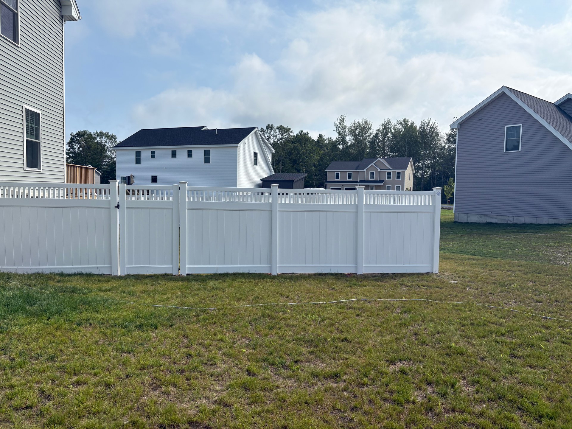A white fence is in the middle of a grassy field in front of a house.