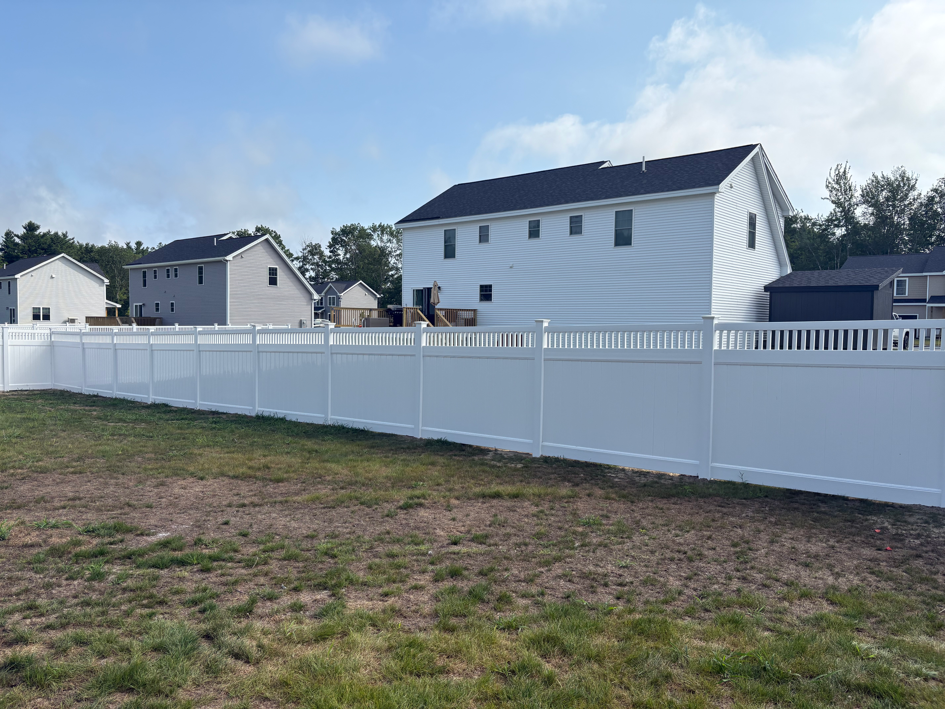 A white fence surrounds a grassy field in front of a house.