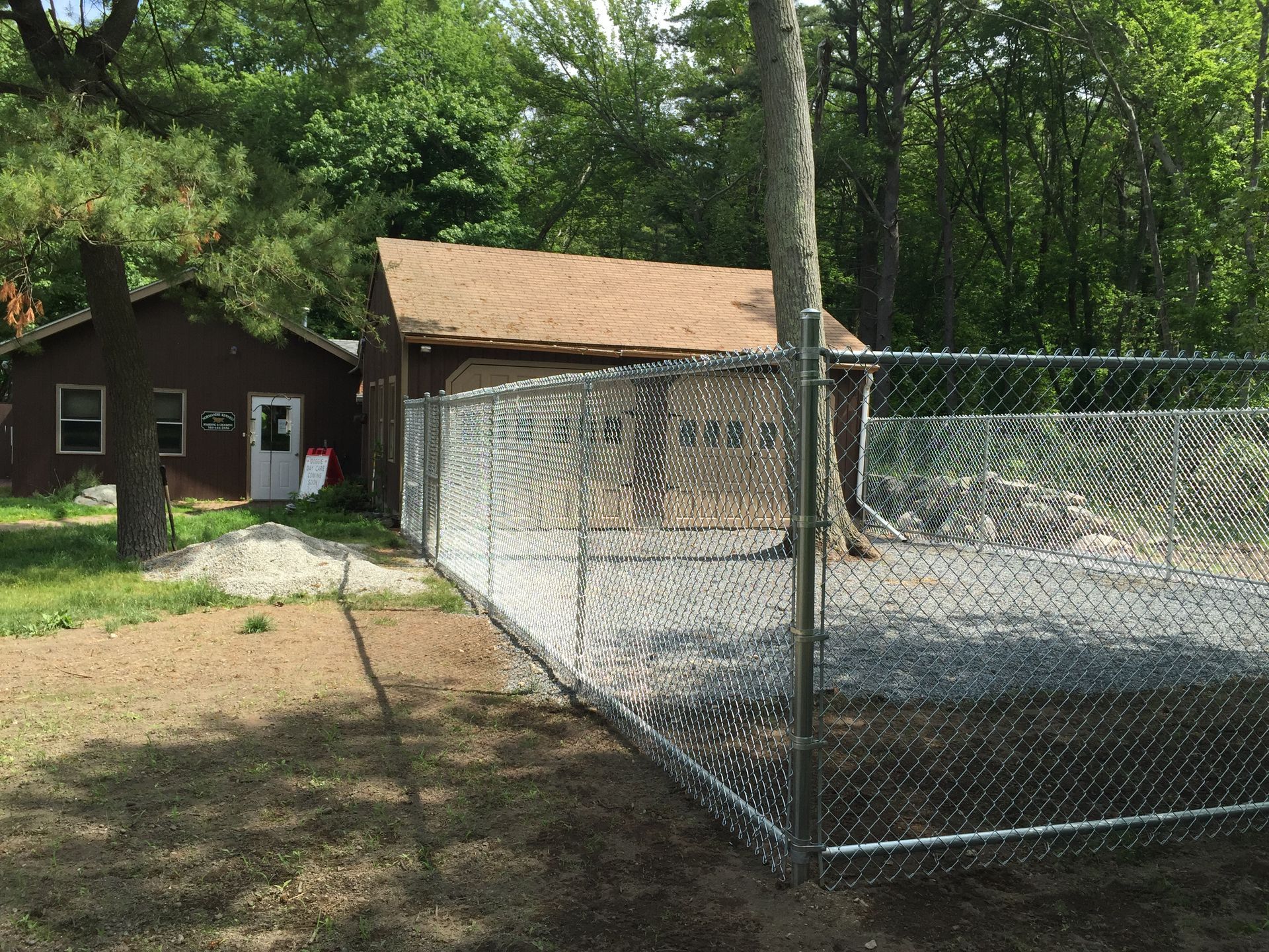 A chain link fence is surrounding a house in the woods.