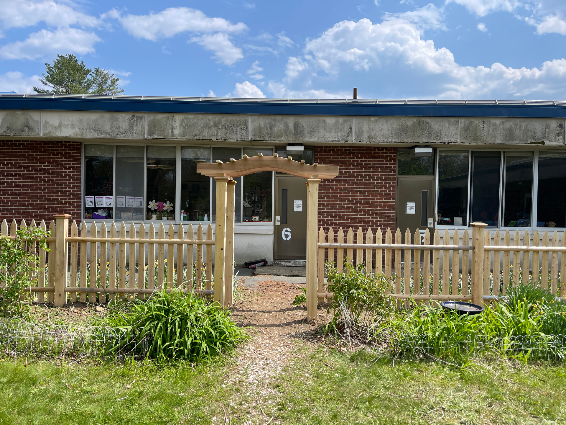 A wooden picket fence is in front of a brick building.